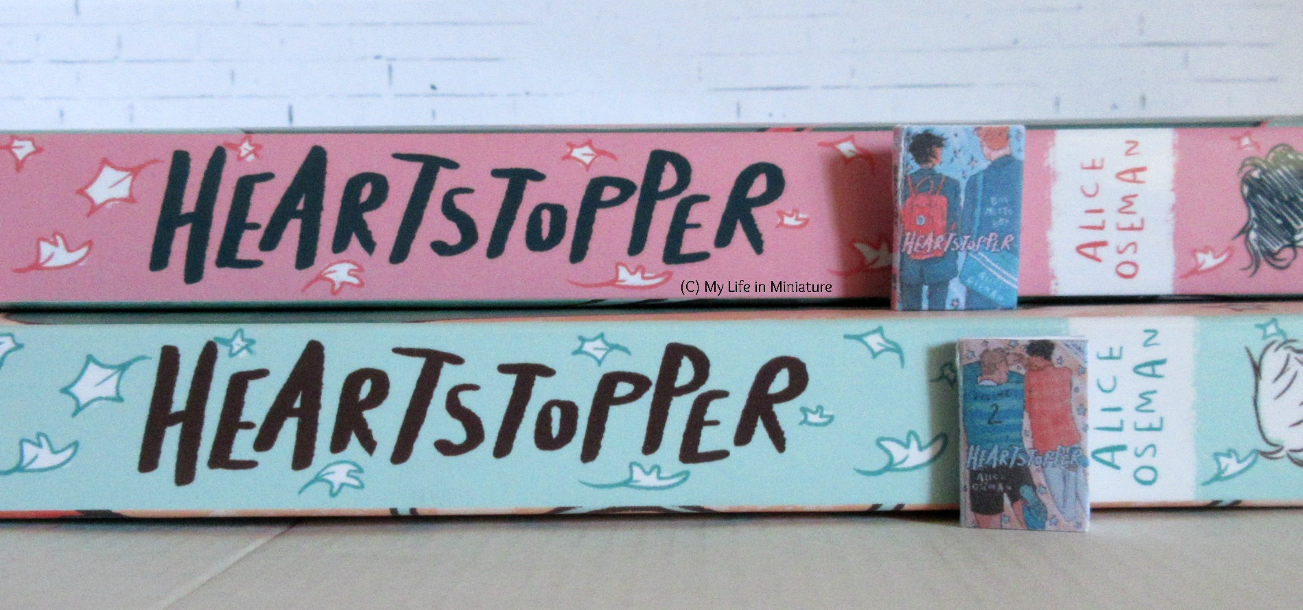 The two life-size Heartstopper volumes are stacked, spines facing the camera. The corresponding miniature version sits next to their matching life-size spines.