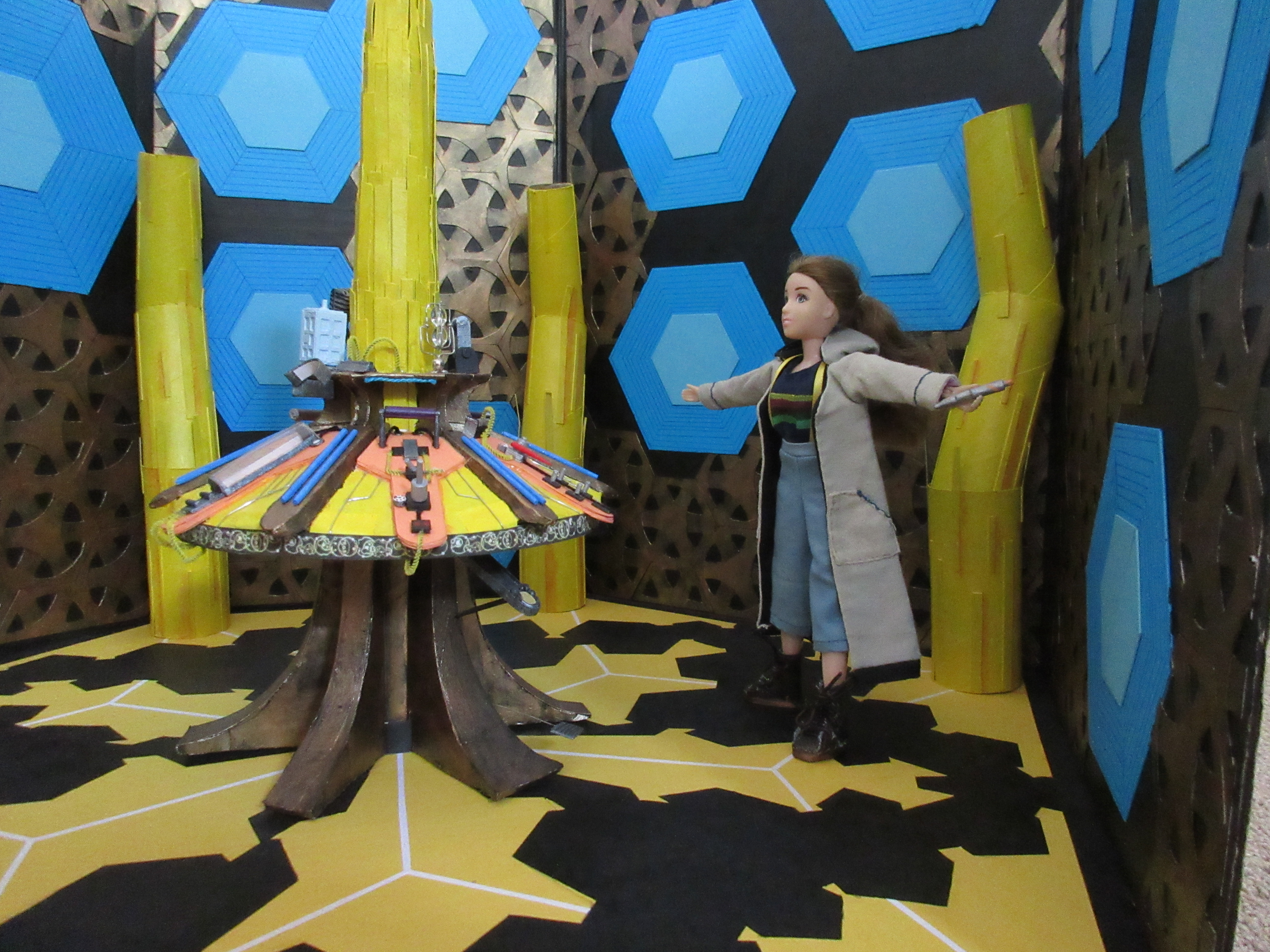 Sarah is in the TARDIS interior set in Thirteenth Doctor cosplay, holding the sonic screwdriver. She stands a distance away from the camera, arms flung wide. She is looking up at nothing in particular.