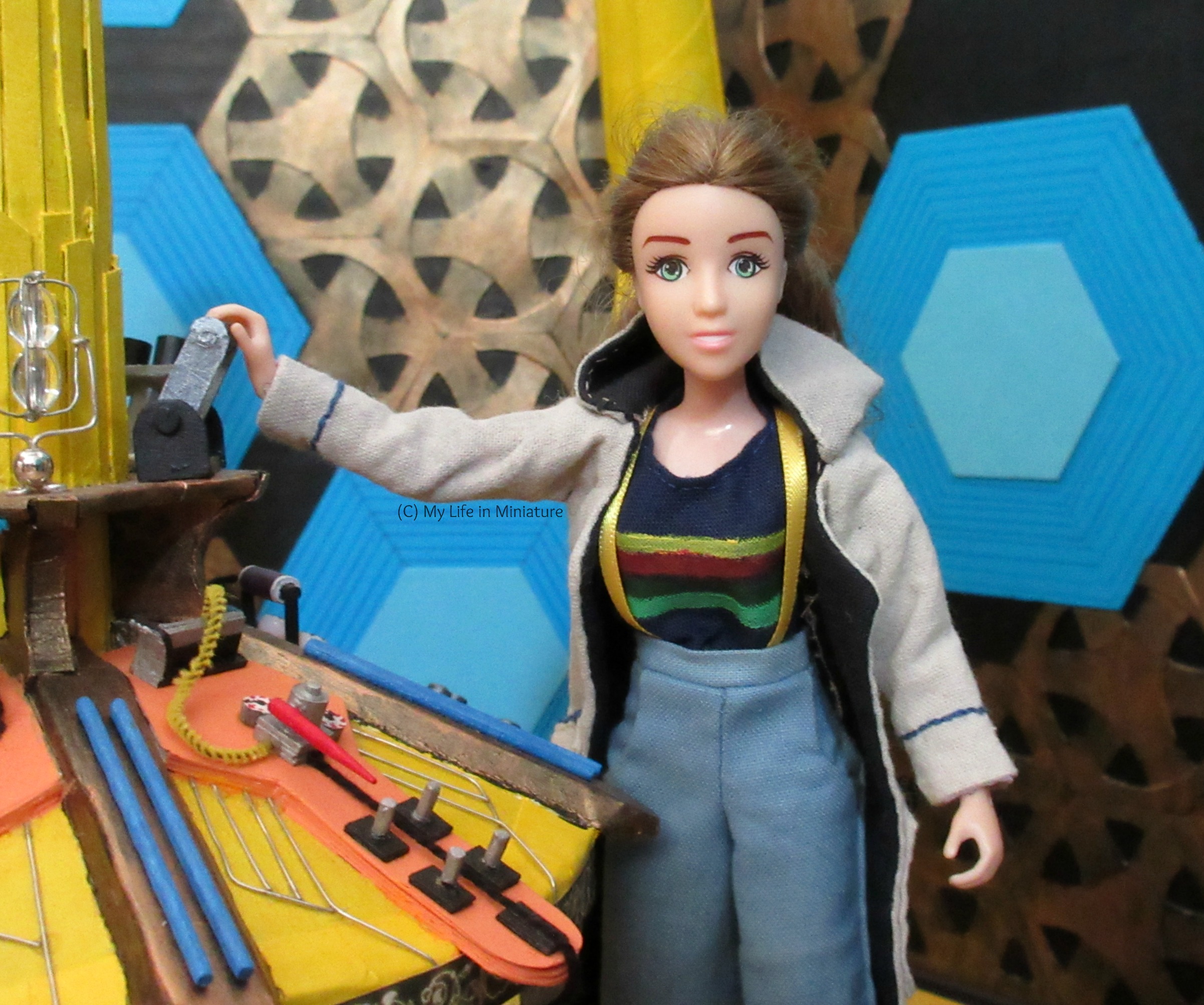 Relative close-up of Sarah at the central console in Thirteenth Doctor cosplay. Her hand is on the dematerialising lever, and she smiles eagerly at the camera. 
