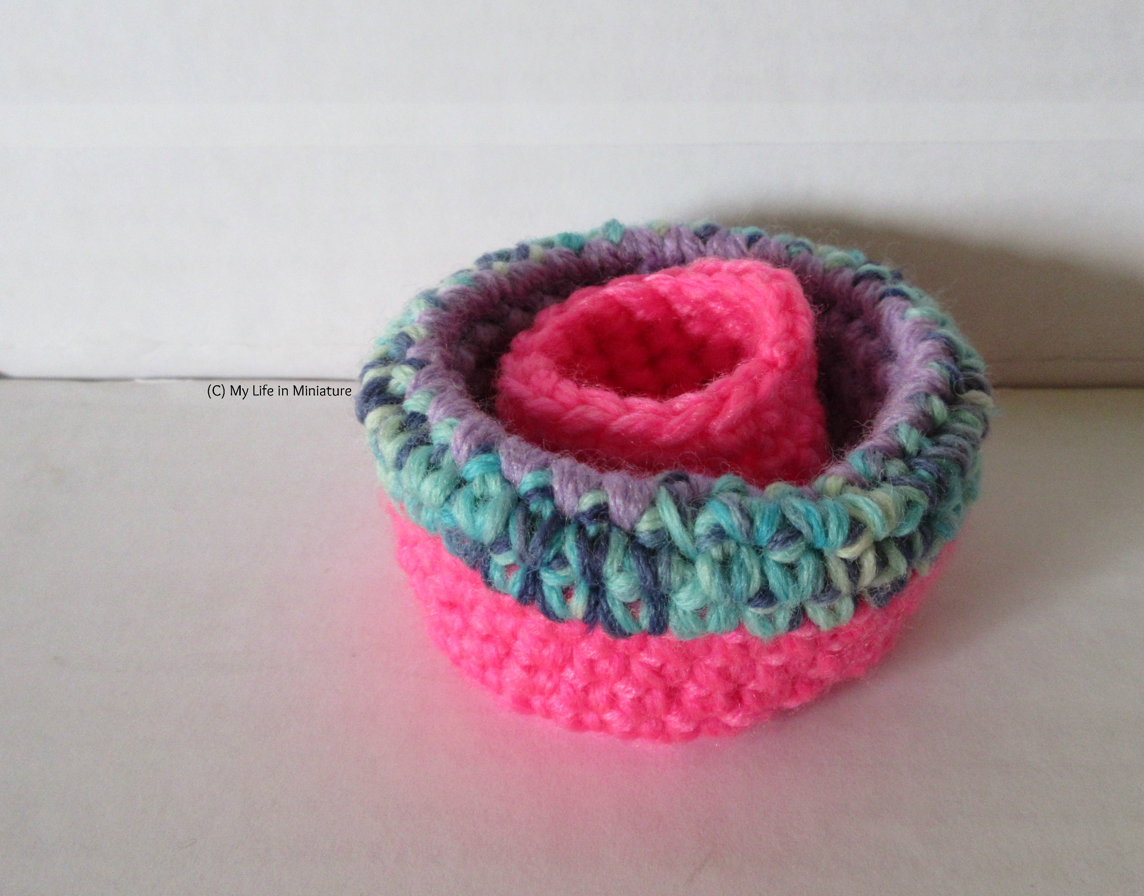 Image shows the larger birds' nest with its sides folded inwards, so the variegated blue yarn is visible. The small hot pink birds' nest is inside the larger one.