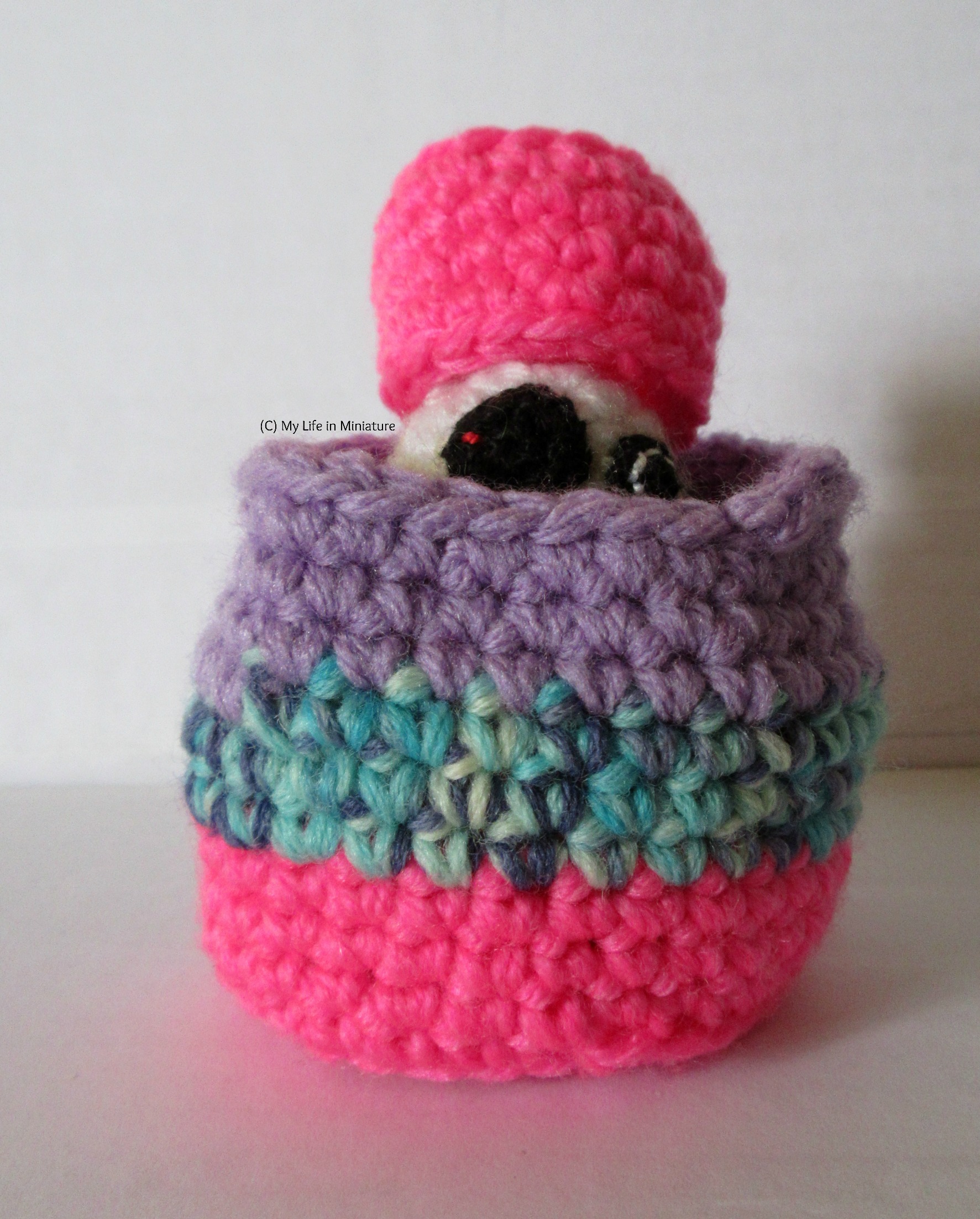 The crocheted BB-8 sits inside the larger nest, with the smaller nest perched on his head like a very large hot pink hat.
