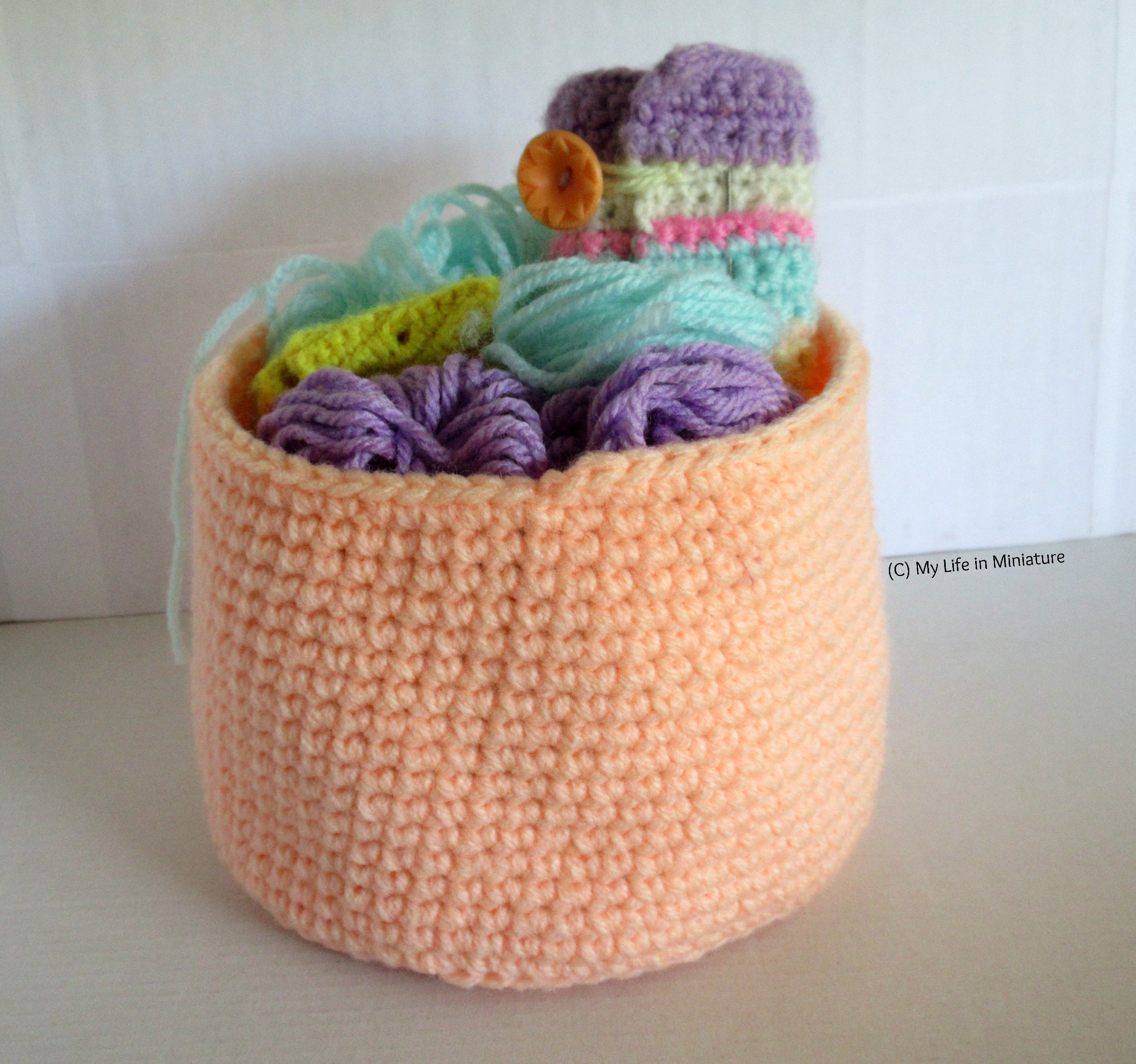 An orange nest sits against a white background, filled with yarn, a crocheted hook roll, and a small yellow pouch holding stitch markers. 