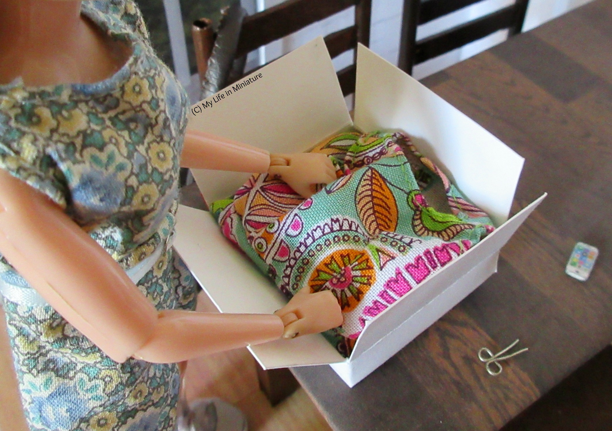 The parcel is fully open, and inside is the bodice of a garment. Sarah's hands reach in to pull it out.