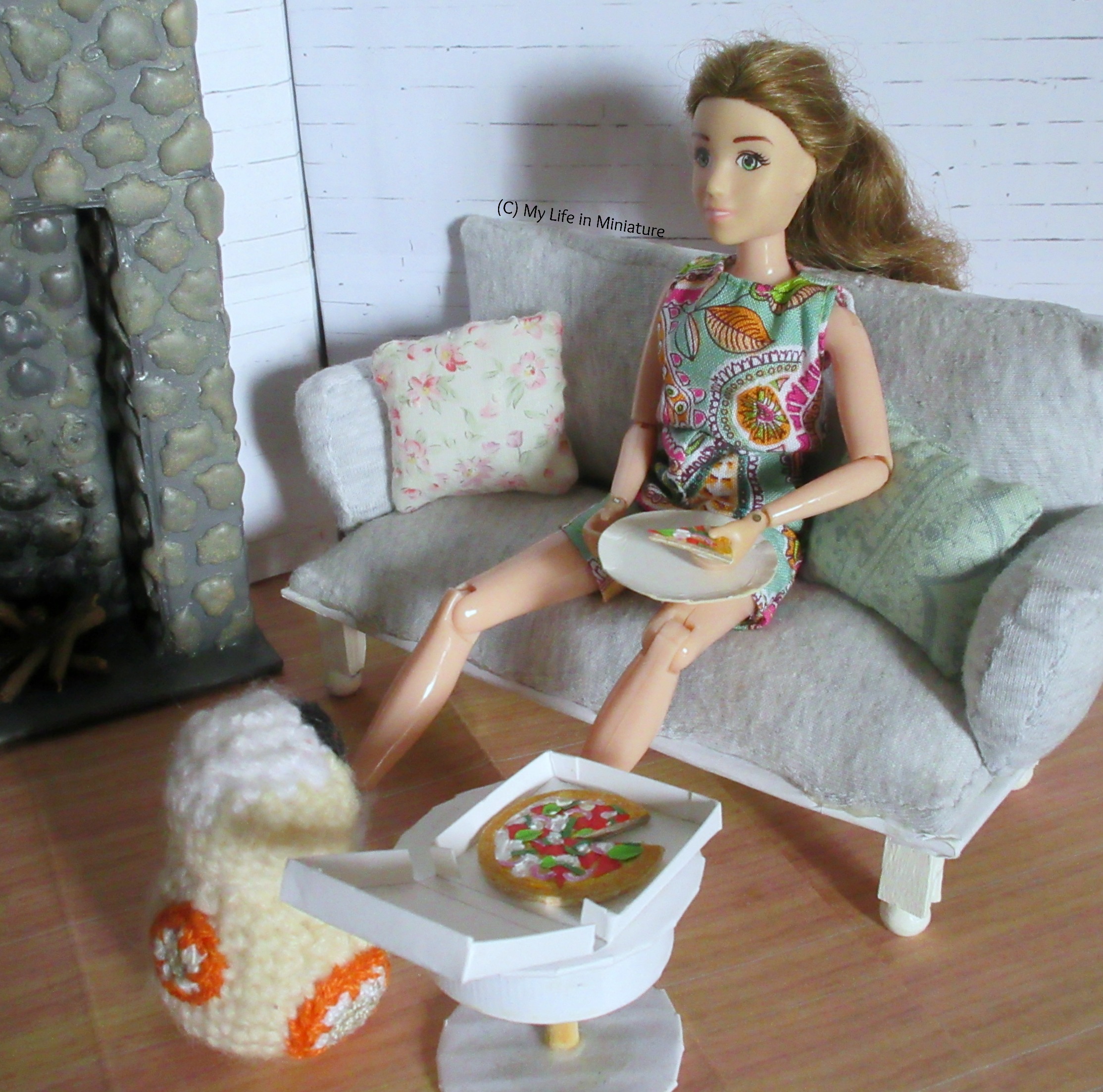 Sarah leans back on her couch, pizza being held over her plate. She is looking at BB-8, who is at her feet staring intensely at the slice. 