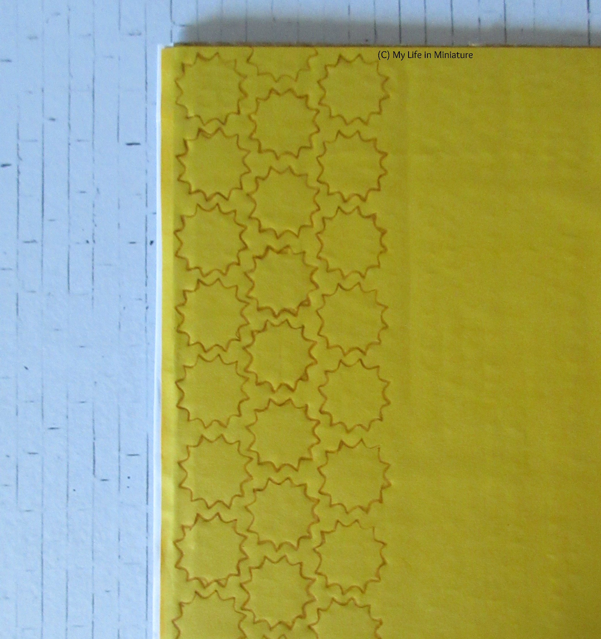 A close-up of a corner of the yellow walls. Three vertical rows of stencilling are done in brown coloured pencil. The shape is a 12-pointed star. 