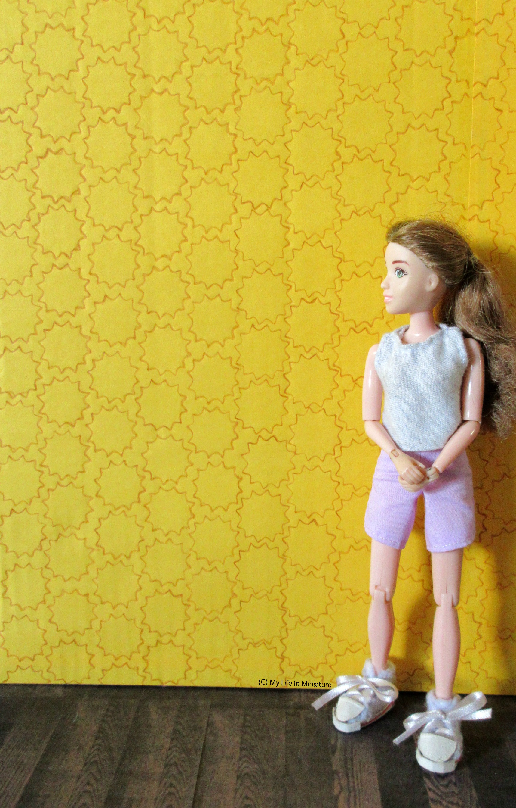 Sarah stands in front of one of the yellow walls, which is covered in the brown stencilled 12-pointed-star pattern. 