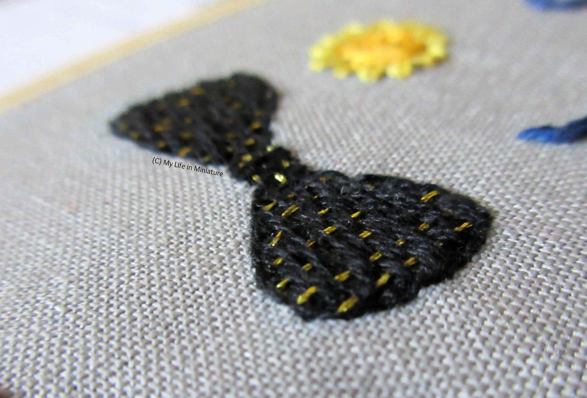 An even closer-up shot, taken from an angle, of the bow tie motif. The woven effect of the stitching is more visible.