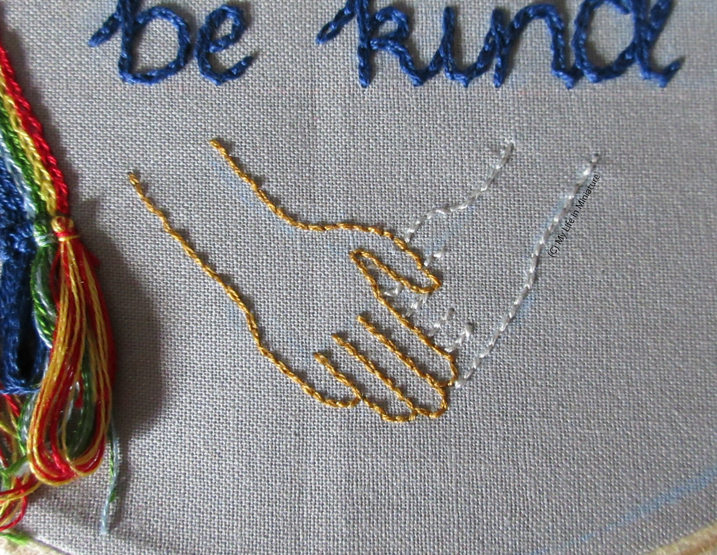 Image shows the bottom of the grey hoop. The gold hand from the image before is visible, now interlocking with another hand, outlined in silver.  