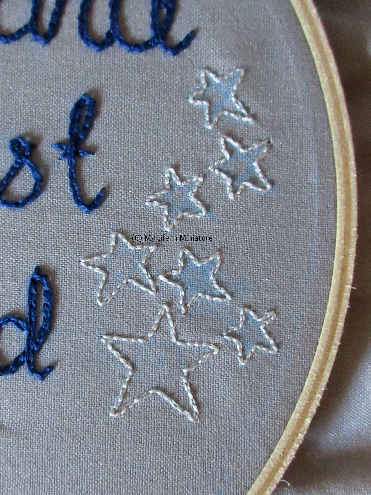 The right hand side of the grey-fabric-filled embroidery hoop is visible. Seven stars are outlined in backstitch in silver, scattered in a loosely vertical manner. 