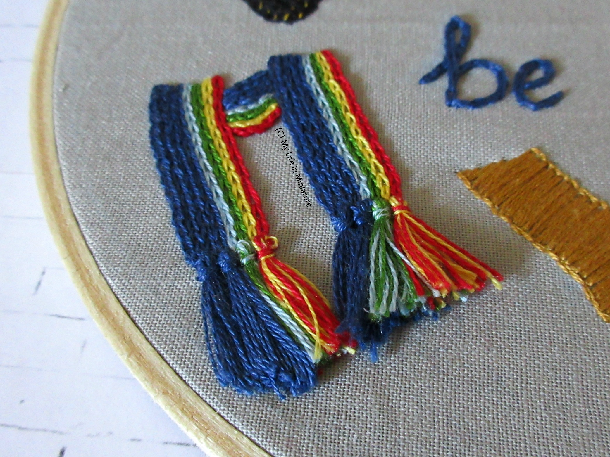 Close-up of the tassels on the rainbow-striped scarf on the left side of the hoop. The tassels are now shorter and neater. 