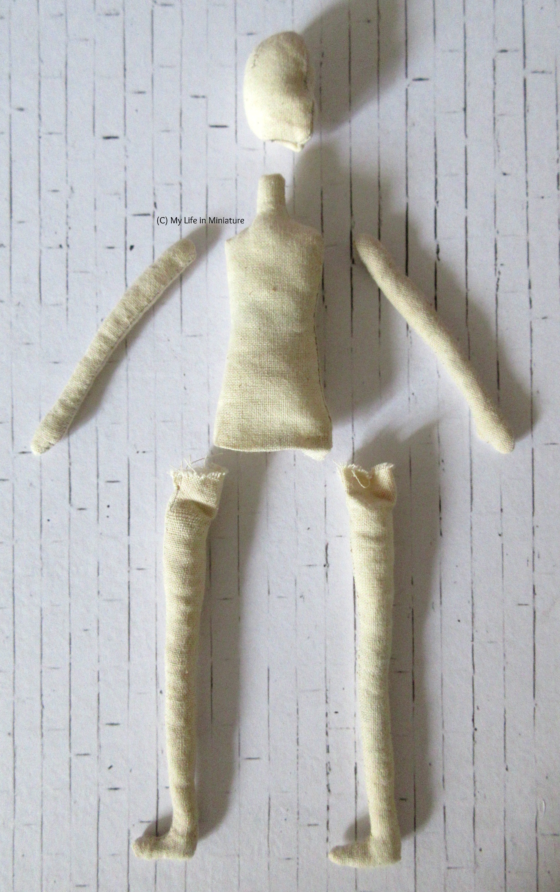 All the completed parts to a muslin doll are laid out on a white brick background, roughly in position to make a doll. 