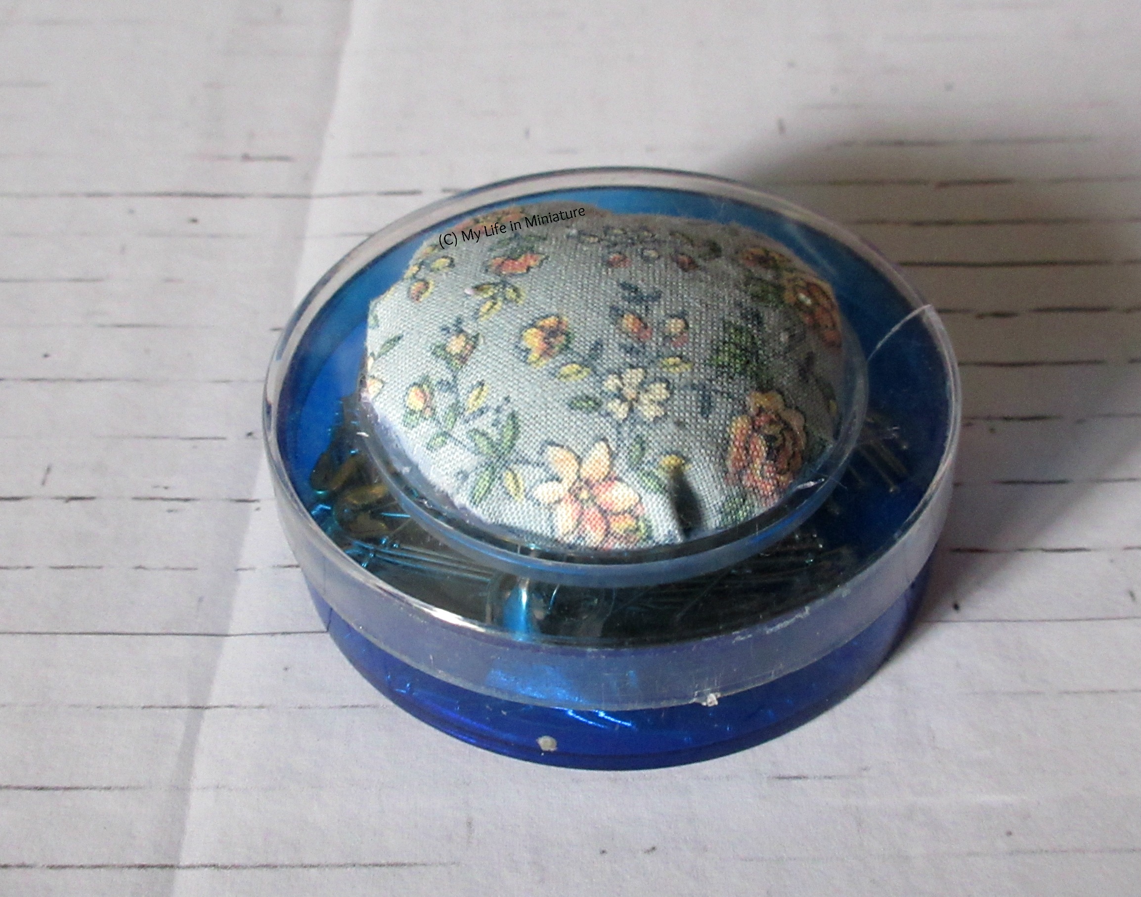 The same blue pin tin from last image, but instead of a yellow sponge in the centre is a circle of blue floral fabric, stuffed in a dome.