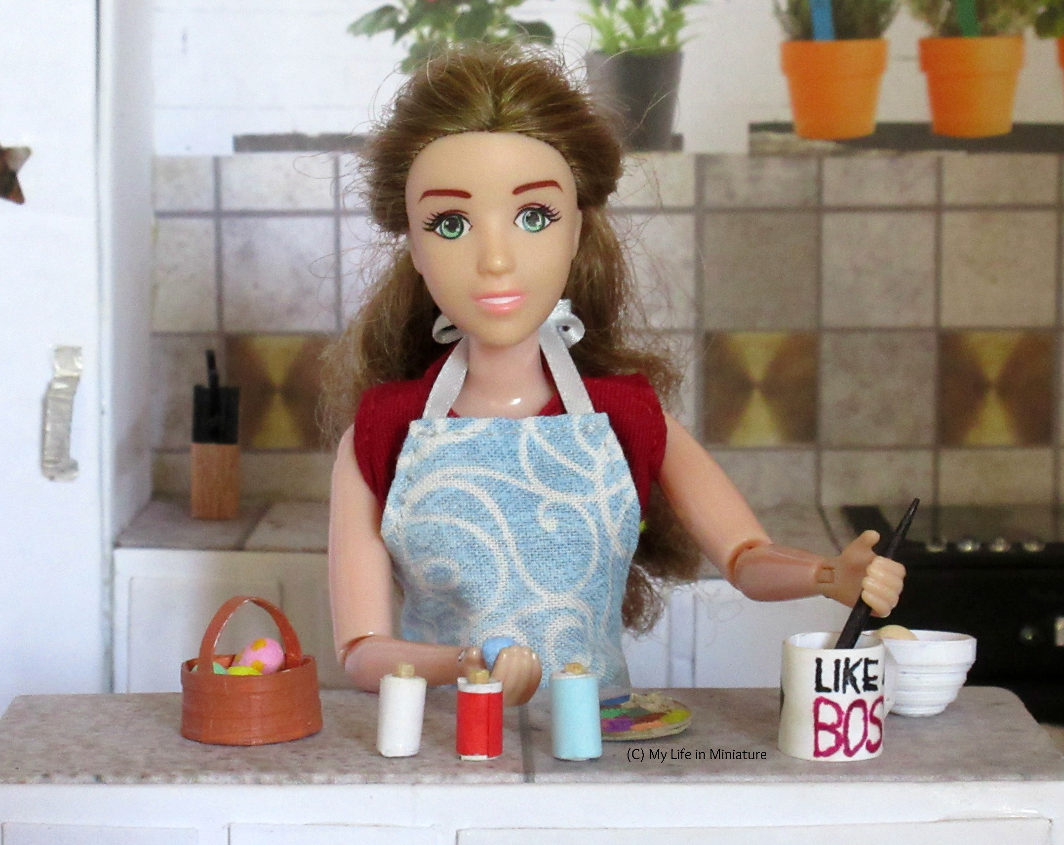 Sarah at her kitchen island, painting eggs in bright colours. A basket of eggs is on her left, and painting supplies are laid out. 