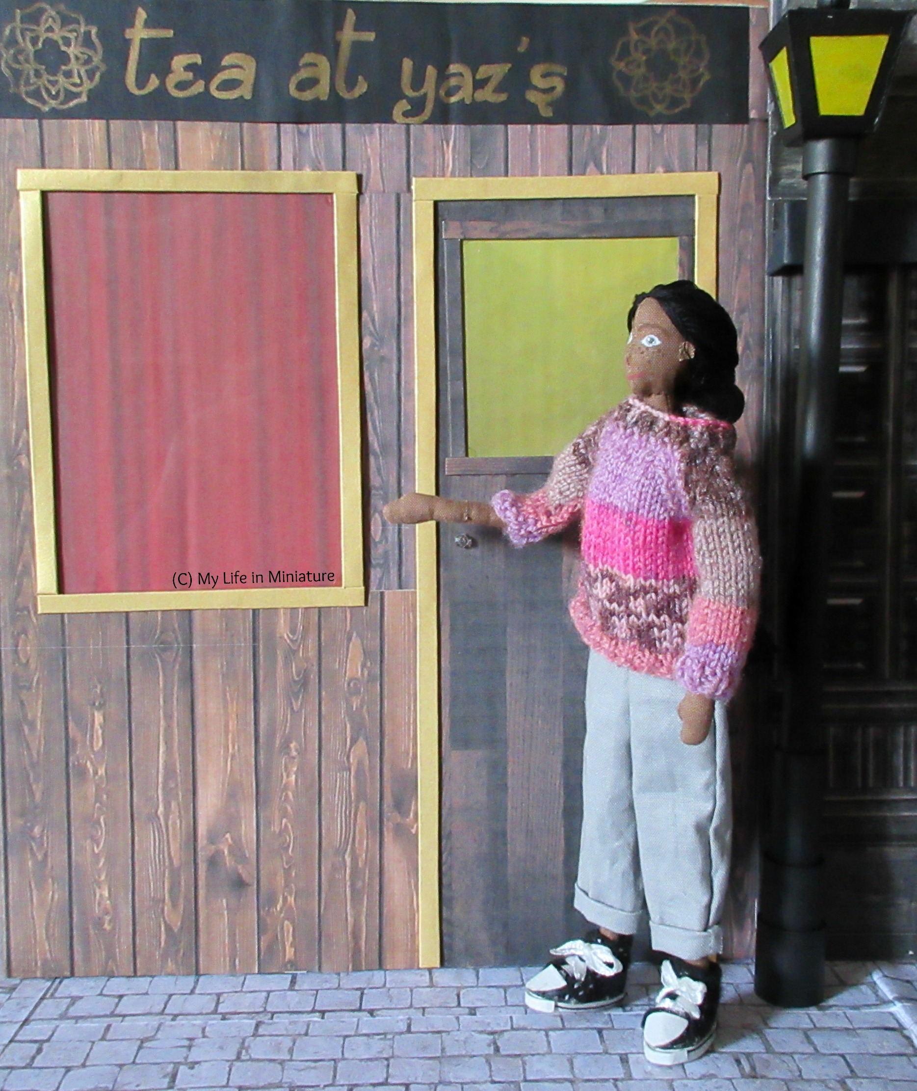 Petra stands in front of Tea at Yaz's, one arm in a 'whala' sort of gesture. She's looking up at the shop name.