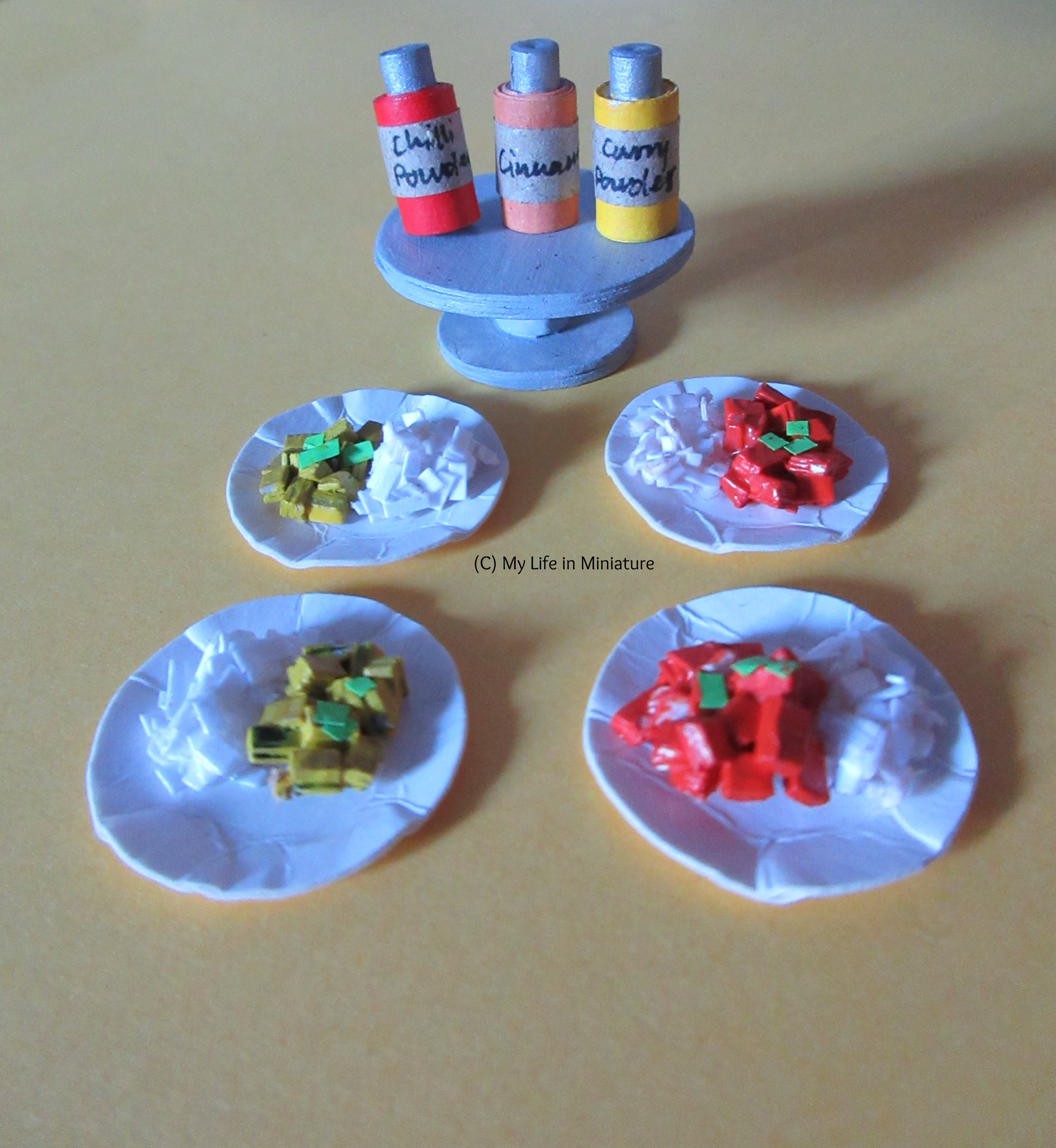 Four plates of curry with rice are on a Tea at Yaz's booth table. A silver cake stand is behind them, with three jars of spices on top.