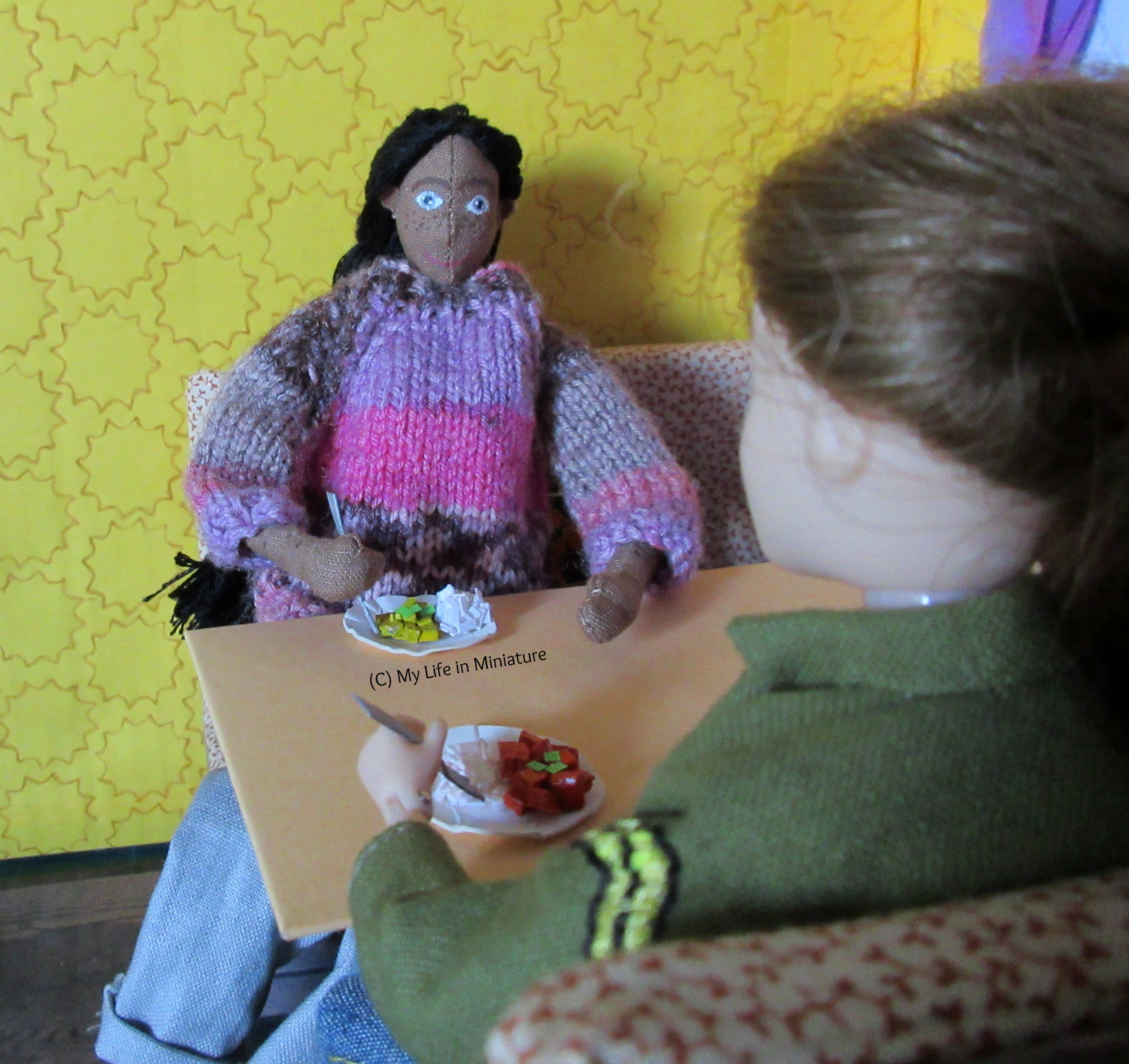 Sarah and Petra sit across from each other at a Tea at Yaz's booth, each eating one of the curries. The photo is taken looking over Sarah's shoulder. 