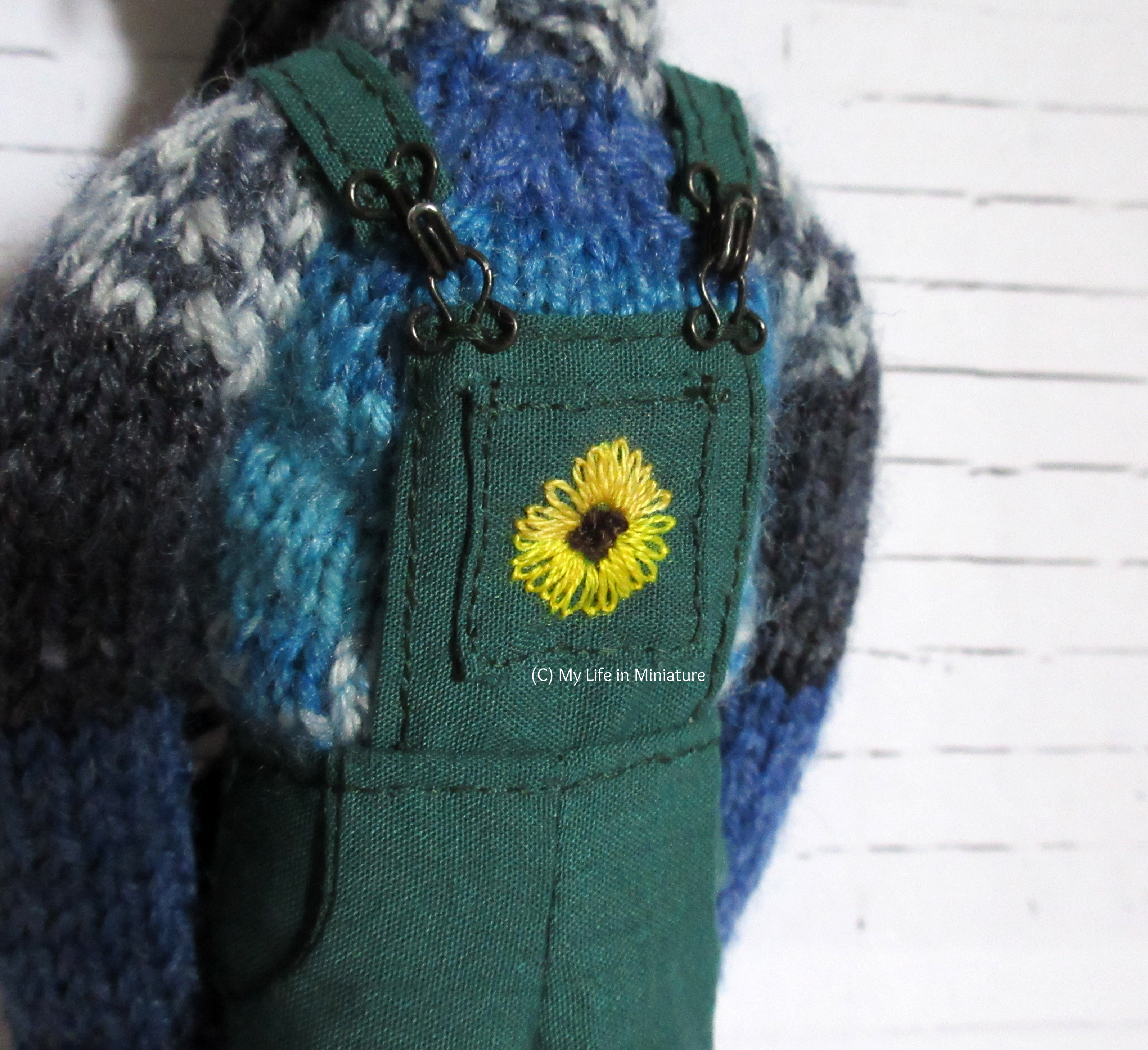 Close-up of the sunflower embroidered on the front pocket of the dungarees. 