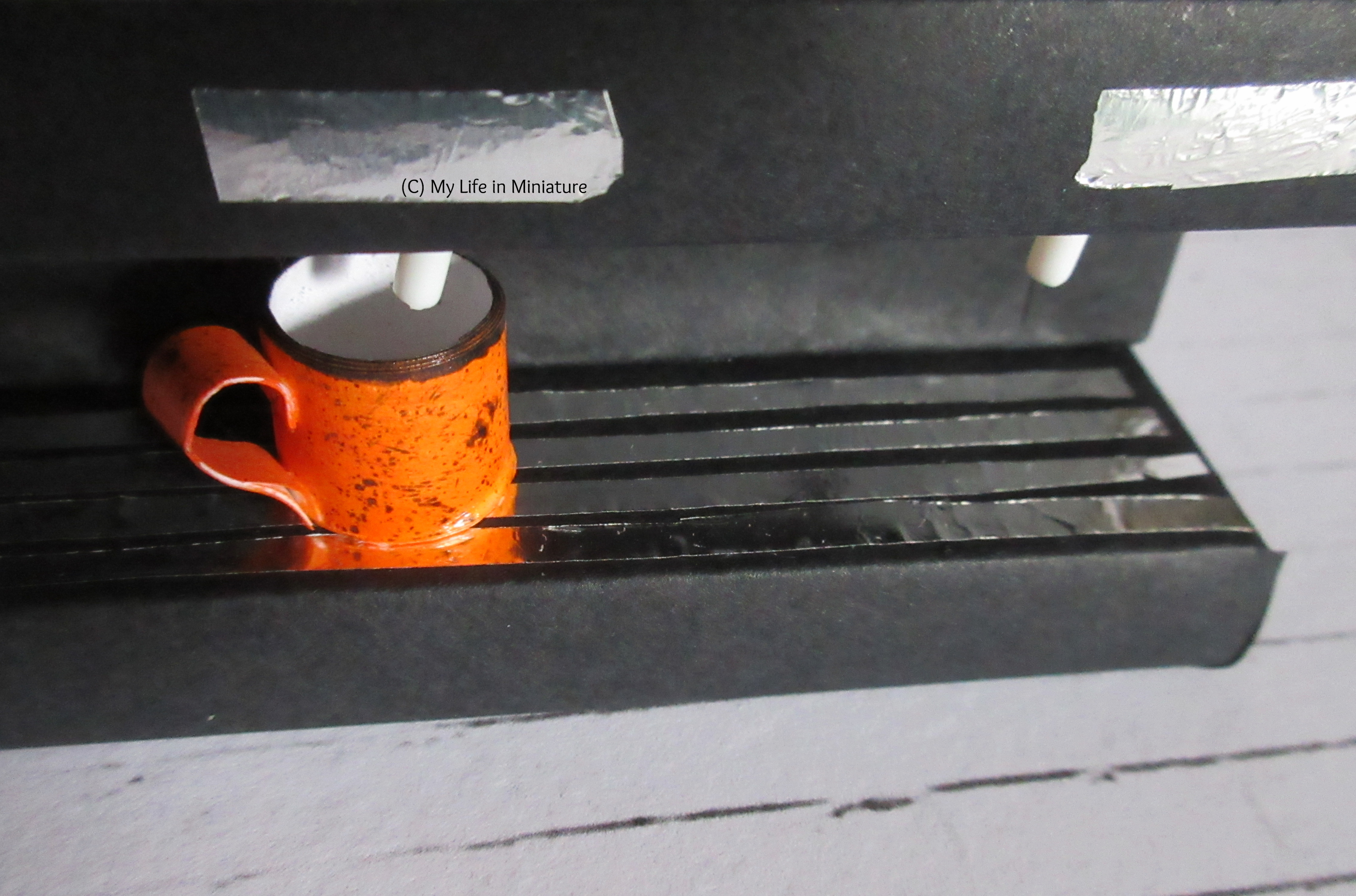 Close-up of the grille underneath the cups, with the orange mug and the control panels visible.