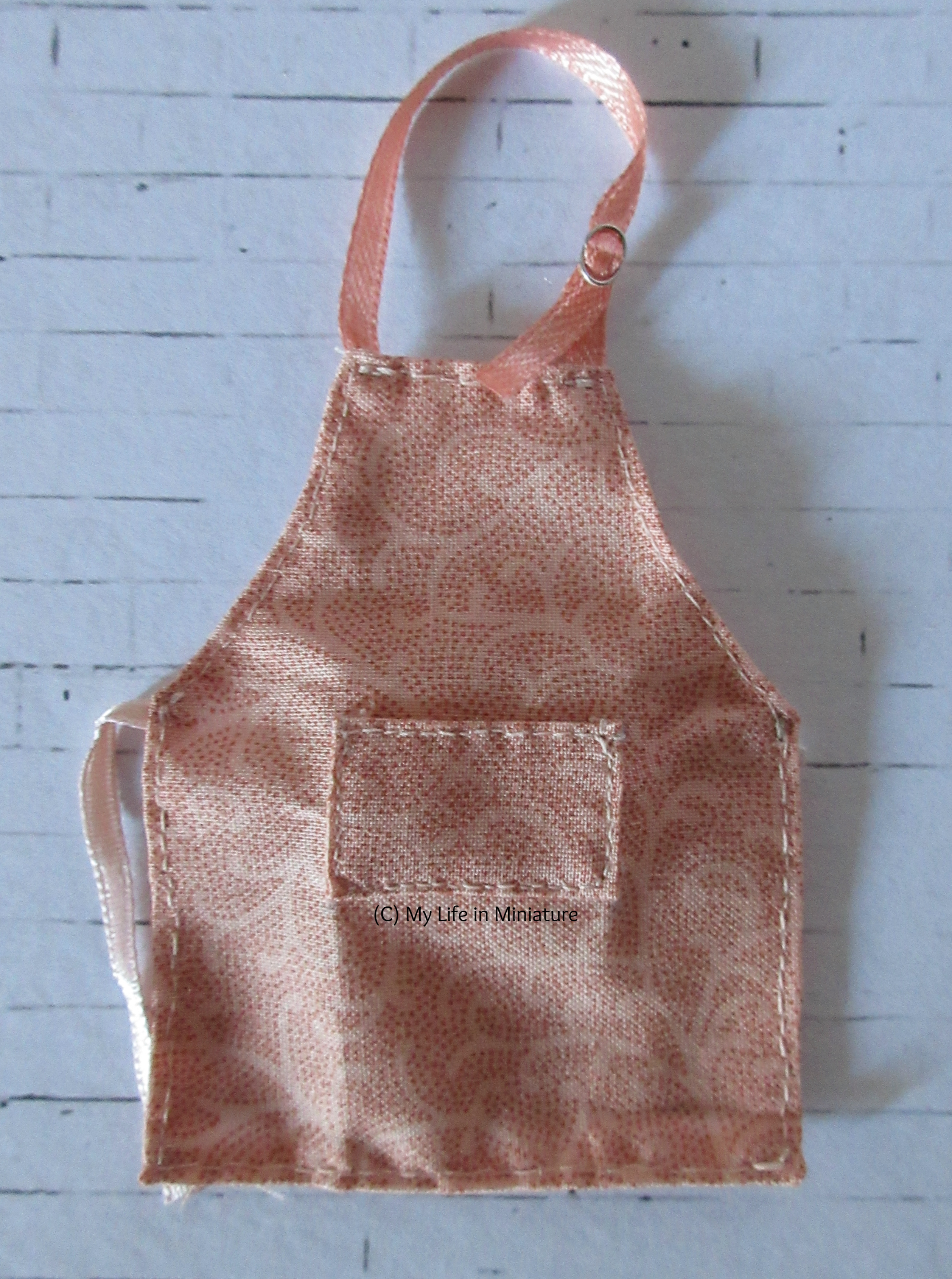 The pink apron sits on a white brick background. 