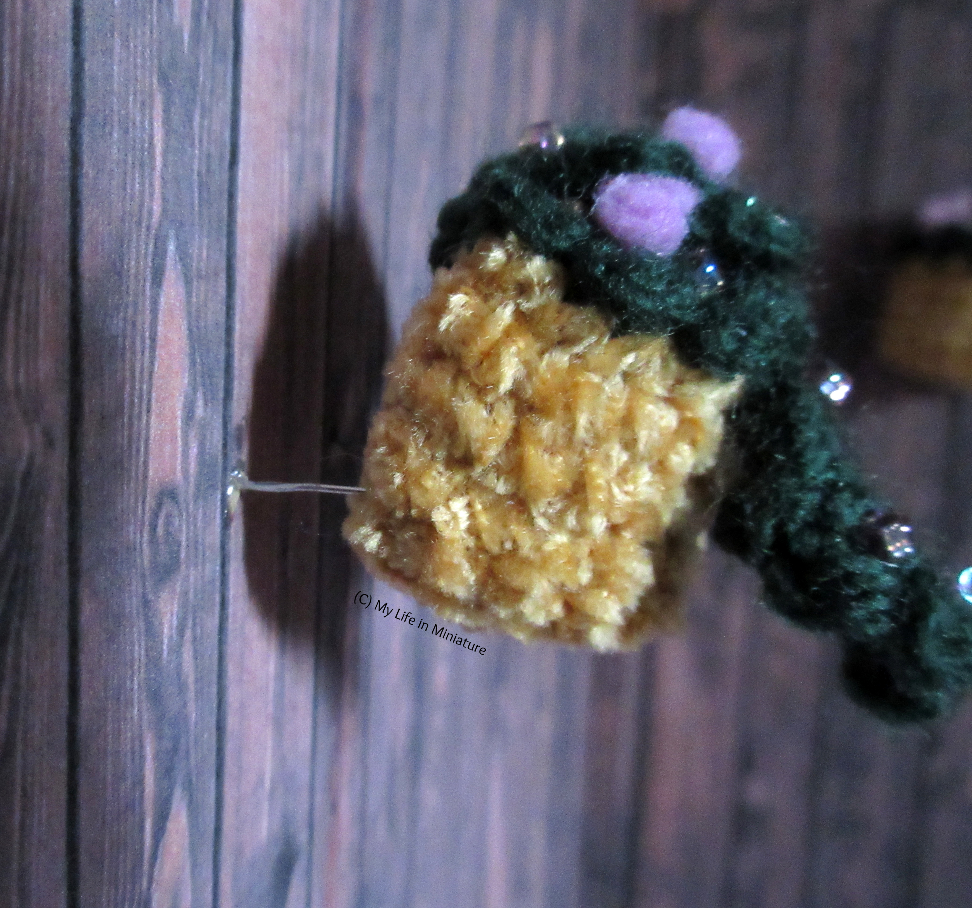 Close-up of the side of one basket on the courtyard wall. There is a wire coming from the wall that goes into the back of the crocheted pot. 