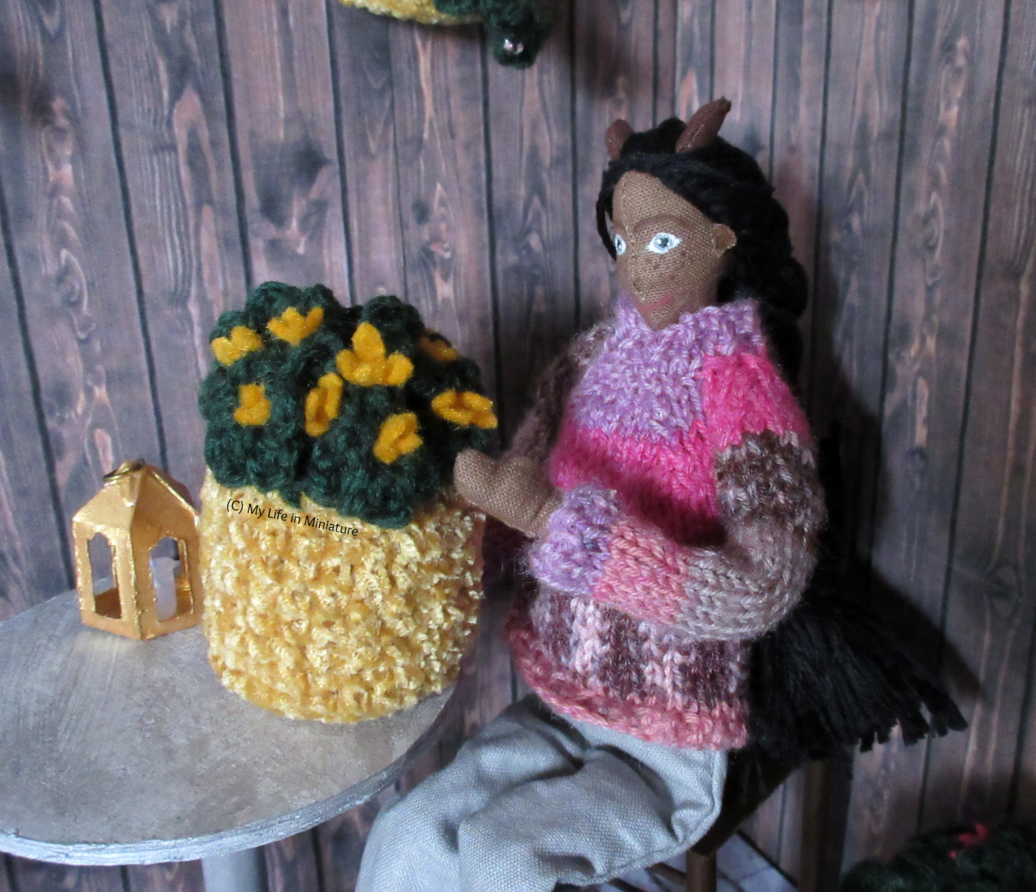 Petra has the pot with orange-yellow flowers on the table in the courtyard. She's examining the leaves and flowers, seated at the table.