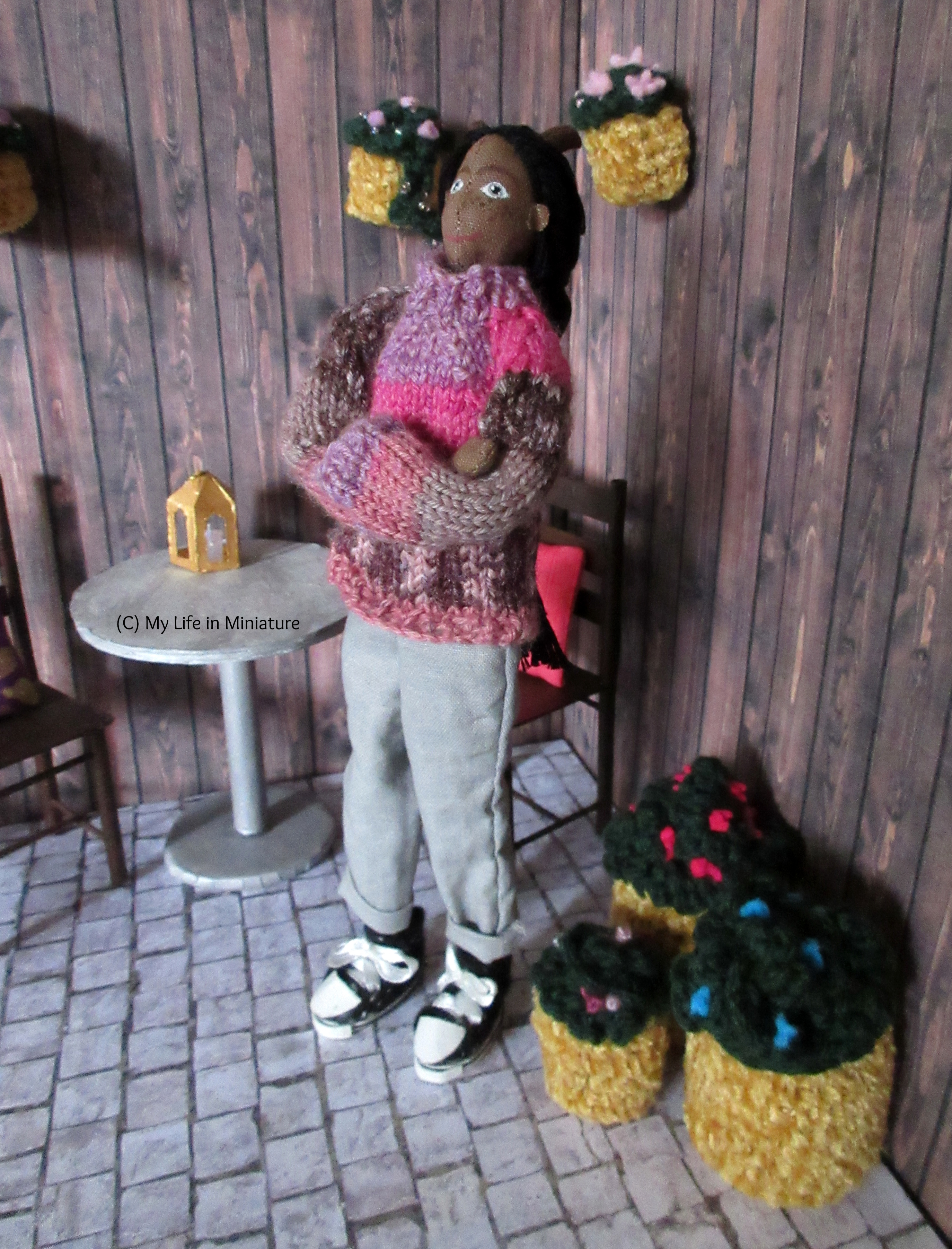 Petra stands in the courtyard next to some of her plants. Her arms are crossed against the chill, and she's looking up at the sky.