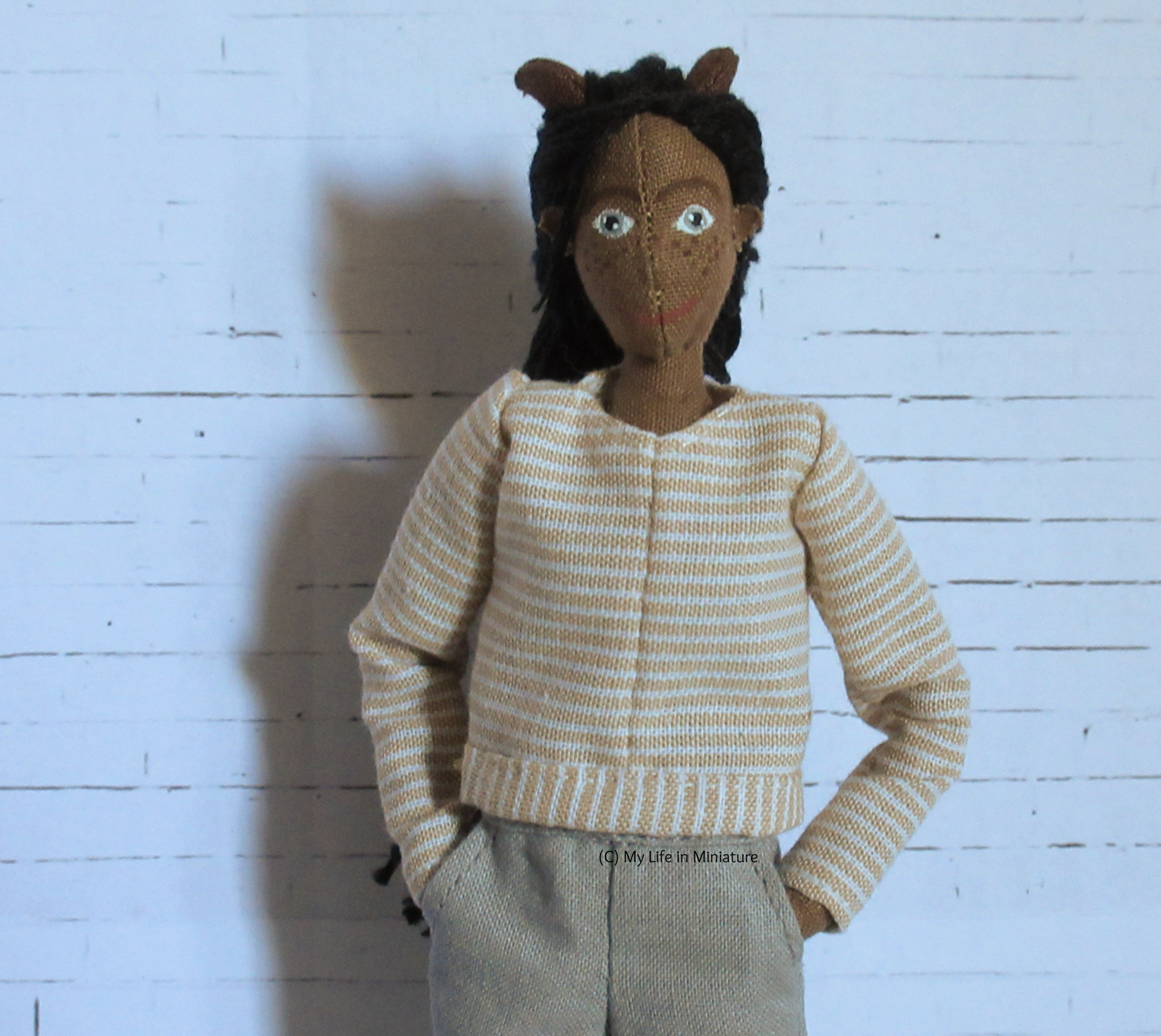 Petra wears a long-sleeved top with her grey pants, hands in pockets. The top is cream-and-white striped, and has a circular neck. 