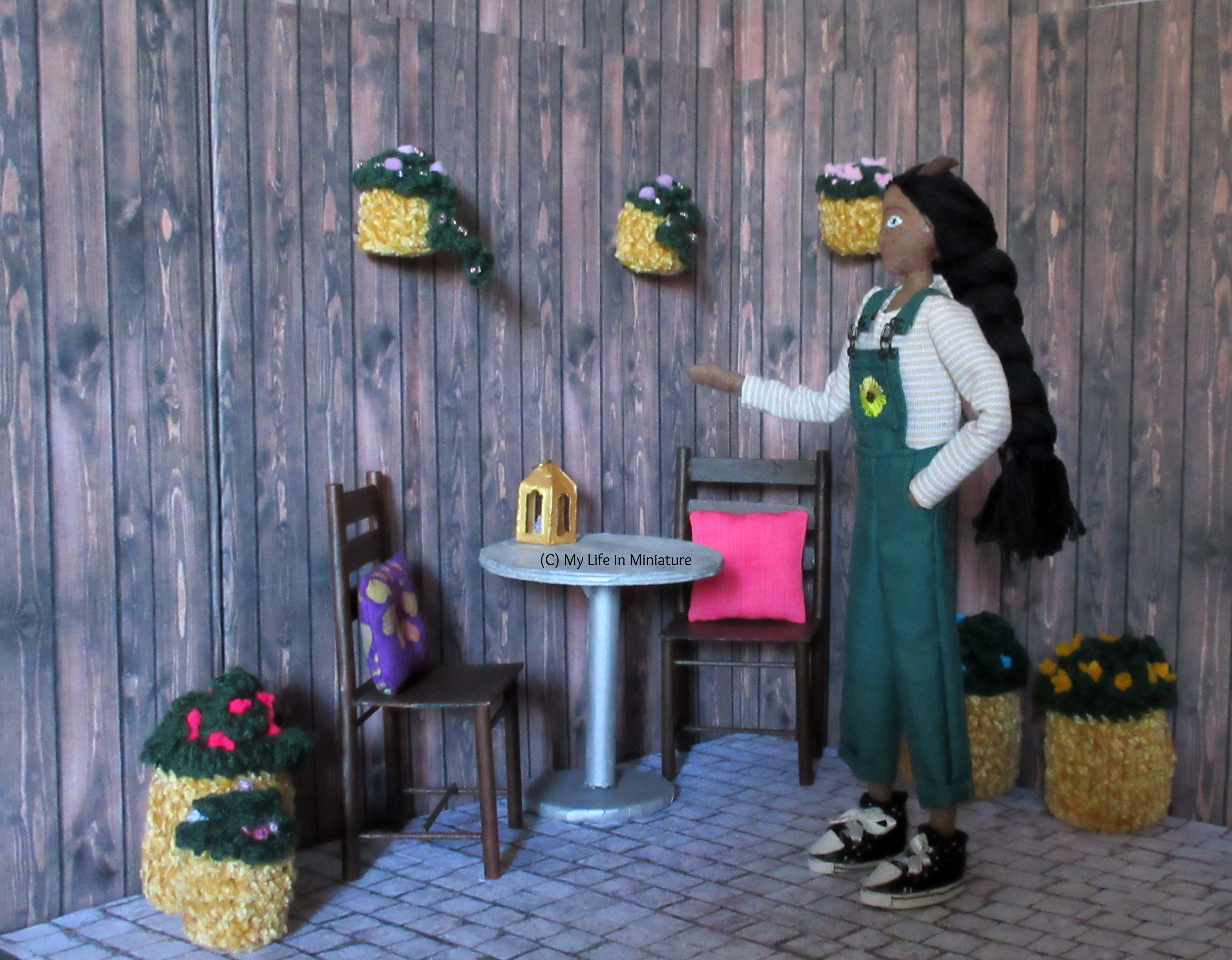 Petra stands in the courtyard of Tea at Yaz's, gesturing around it. She looks to the left. 