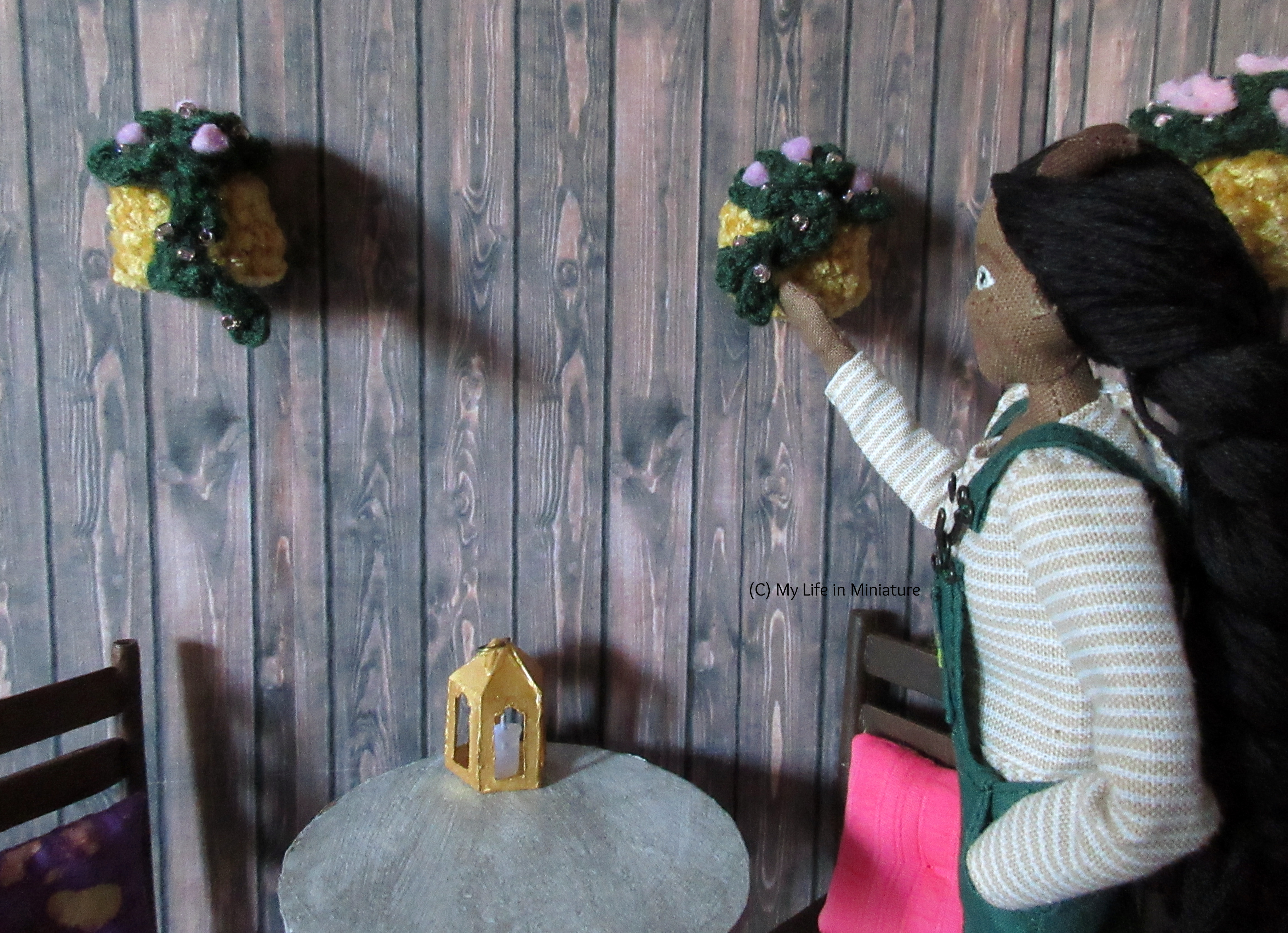 Petra stands near the purple hanging baskets, cupping one of the trailing branches in her hand. She's looking at the leaves she's holding.