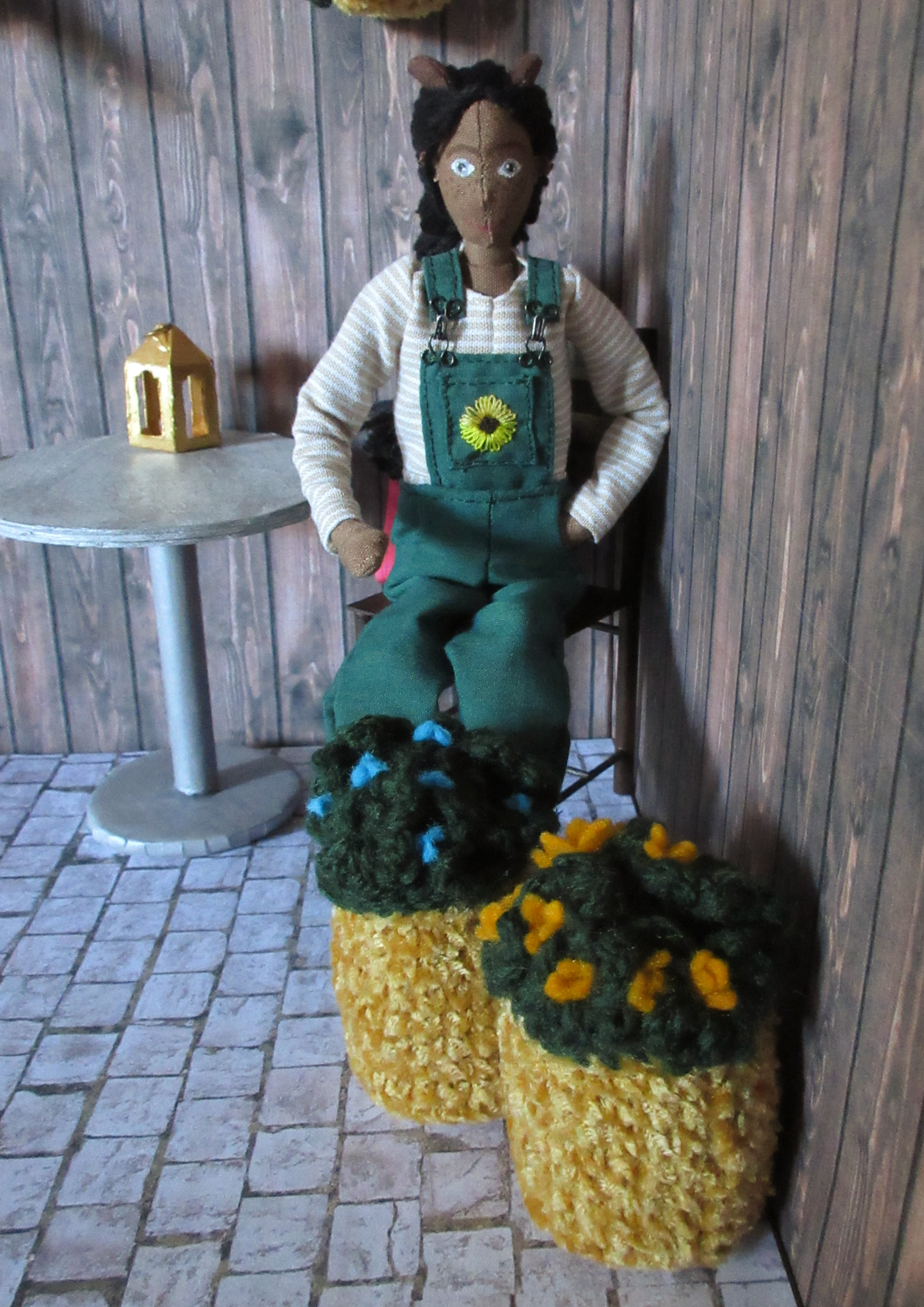 Petra sits on one of the chairs in the courtyard, behind two of the big pots. She's pointing out the different flowers. 