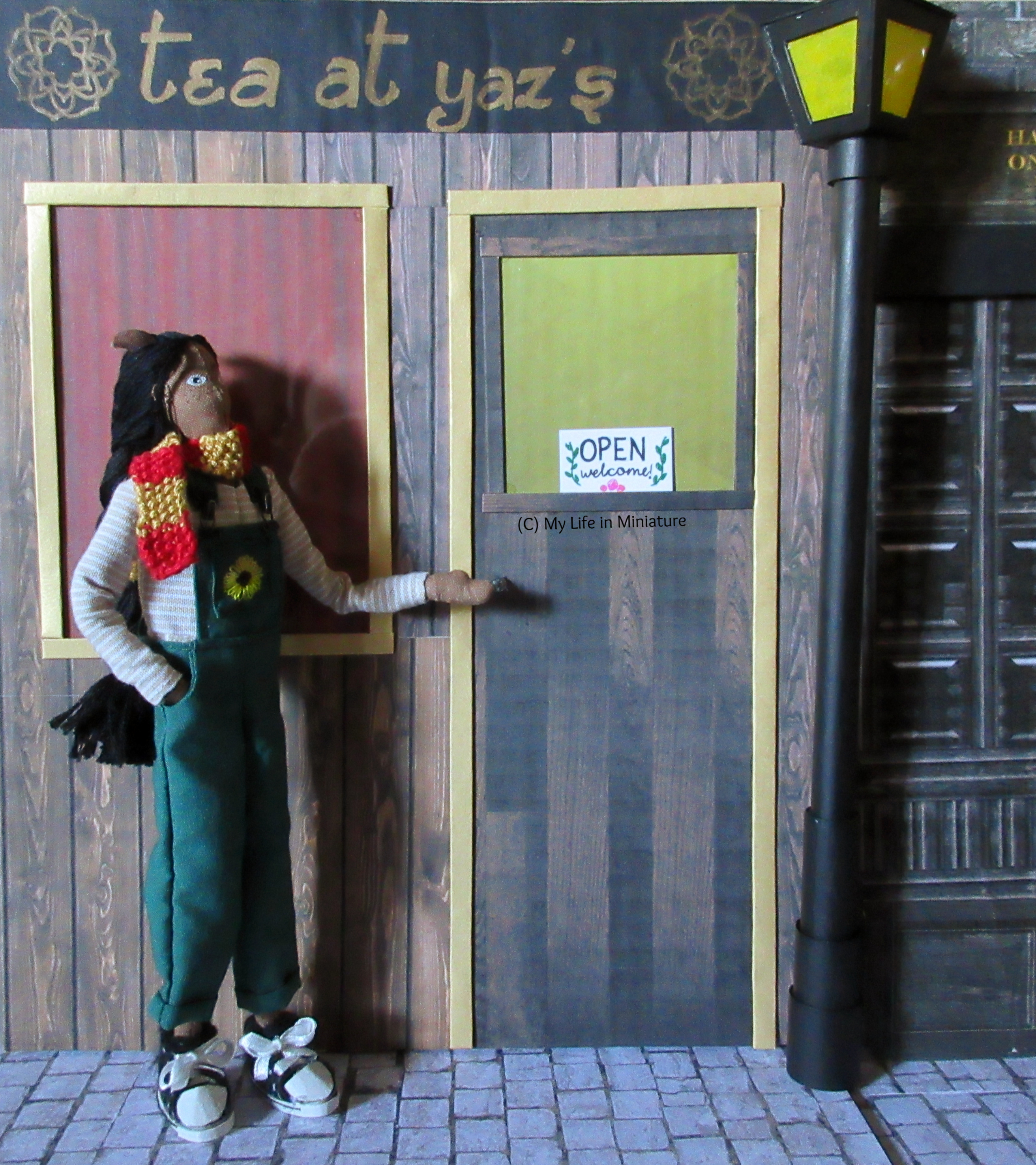 Petra stands outside Tea at Yaz's, gesturing in a 'whala!' sort of manner to the front of the shop. She's looking to the right.