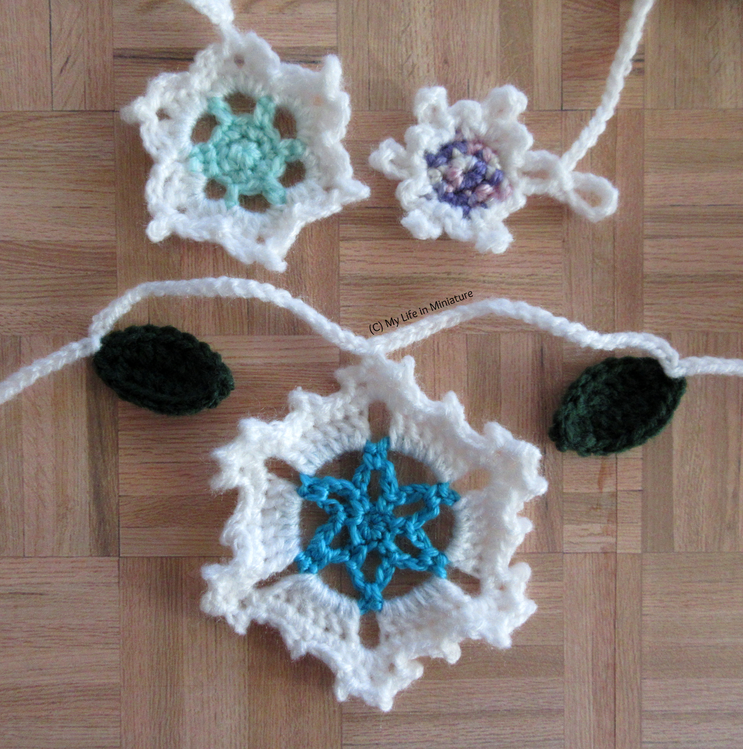 The three sizes of snowflakes and two of the leaves are arranged on a wood parquet background.