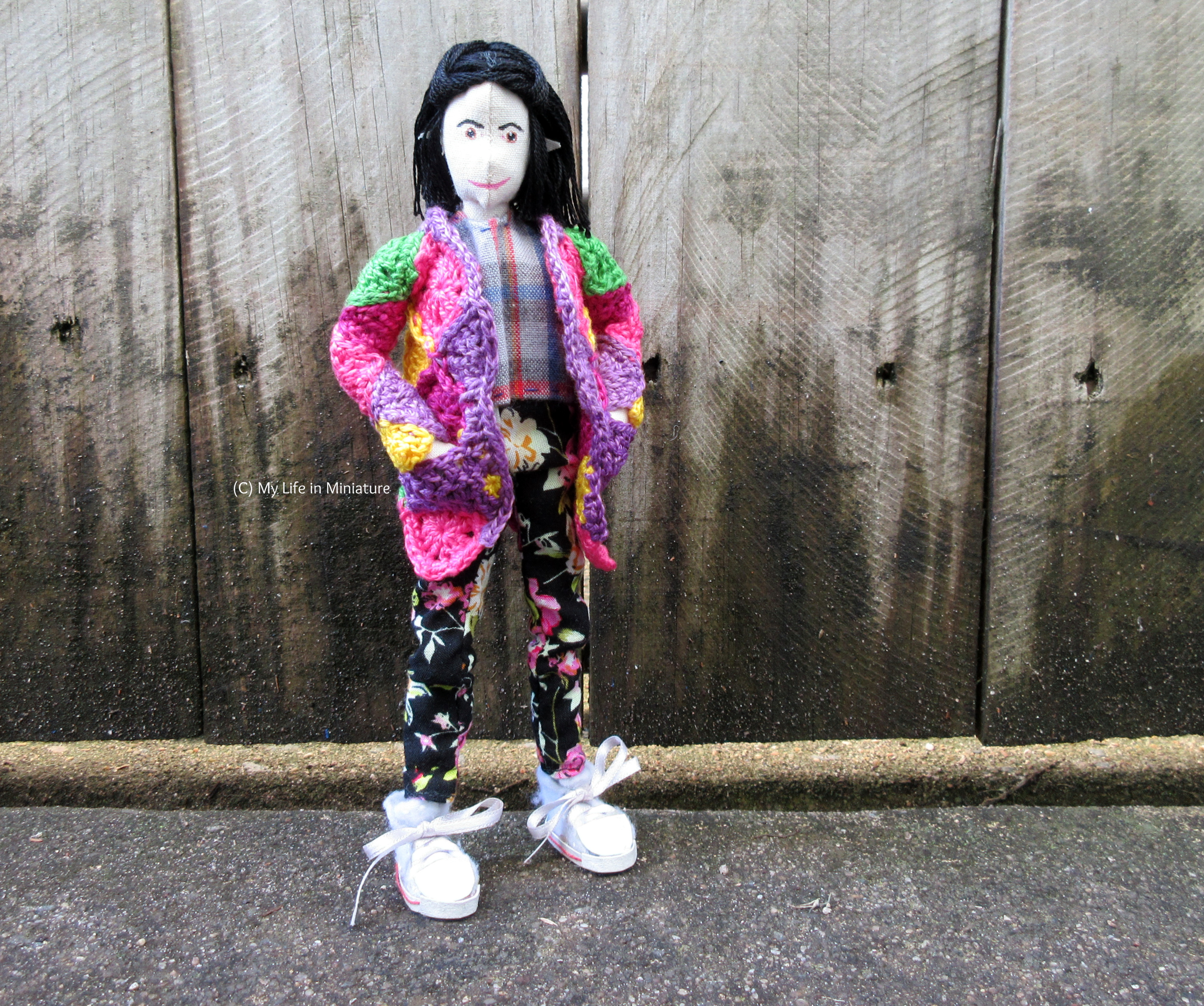 Tiffany stands against a wooden fence outside, smiling at the camera. Her hands are in the pockets of her cardigan.