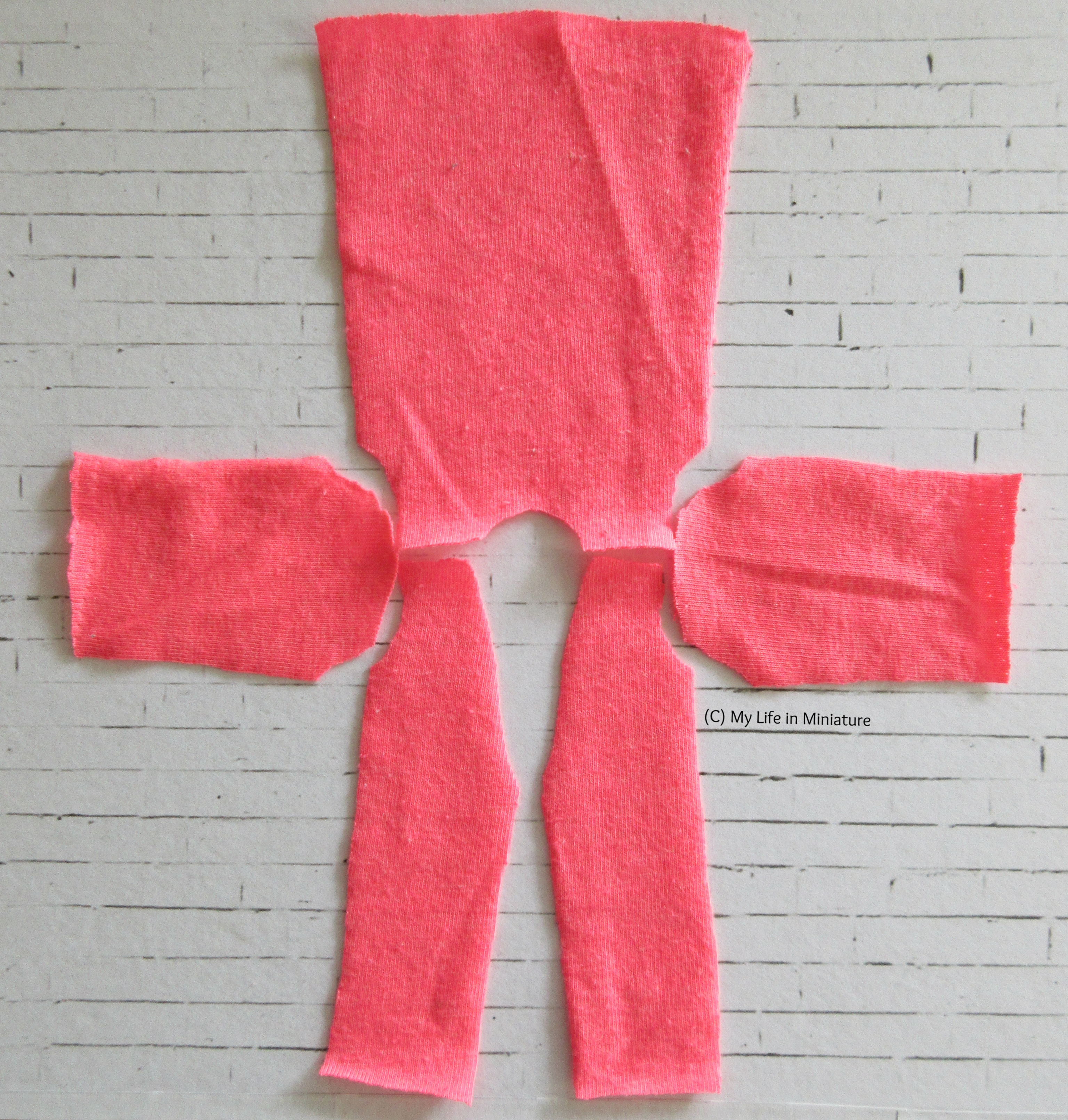 The pieces for a cardigan are laid out on a white brick background in the rough shape of a cross. The fabric is neon pink jersey. 