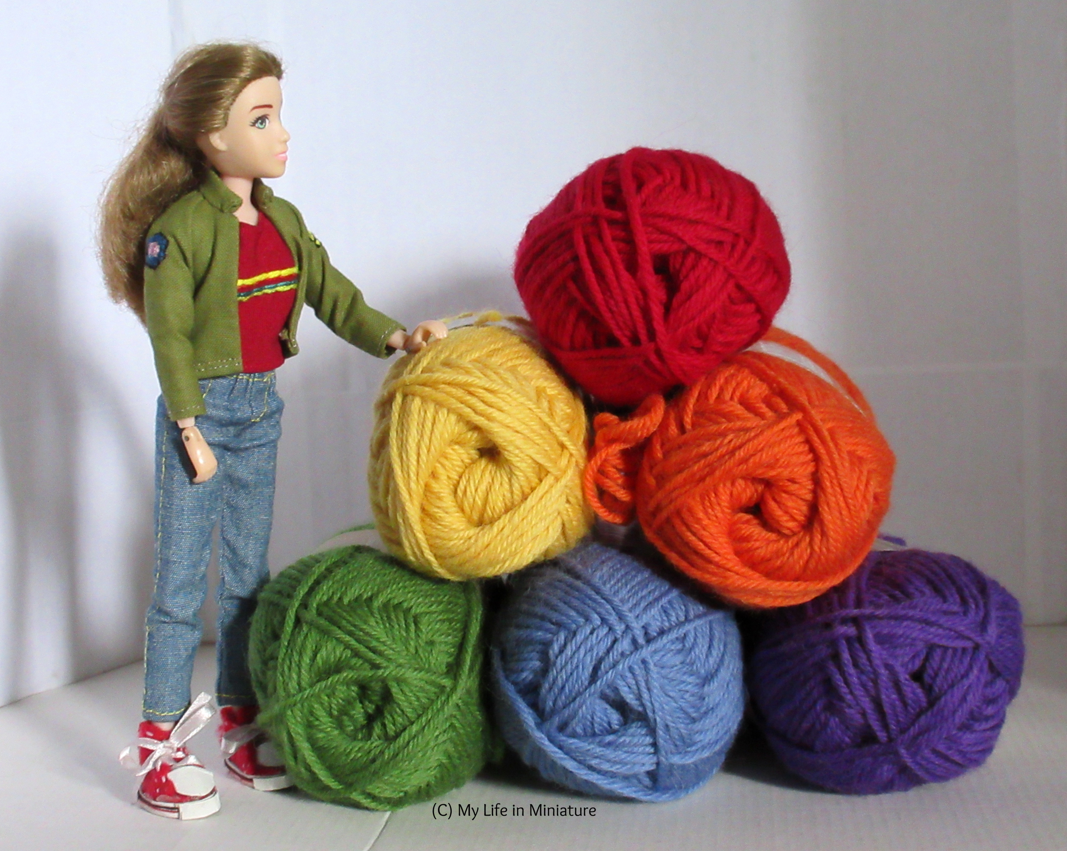 Sarah stands next to a pyramid of stacked balls of yarn. The yarn is in rainbow order from top to bottom. She rests her hand on the closest ball and looks at the top yarn ball.