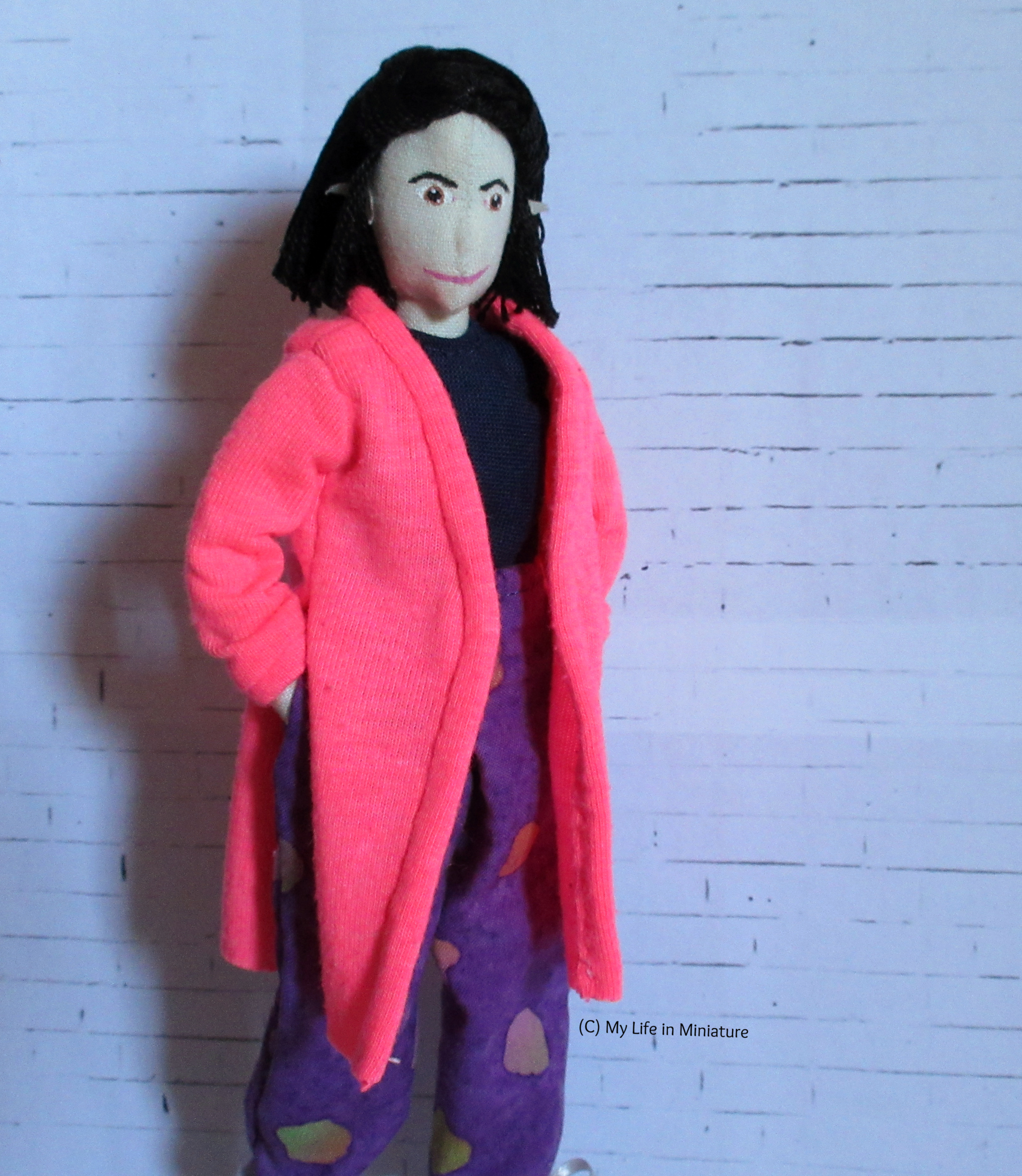 Tiffany wears her neon pink cardigan with her loose purple pants and a navy top. The cardigan goes to her knees, with side seam slits to her waist. Her hands are in her pockets.