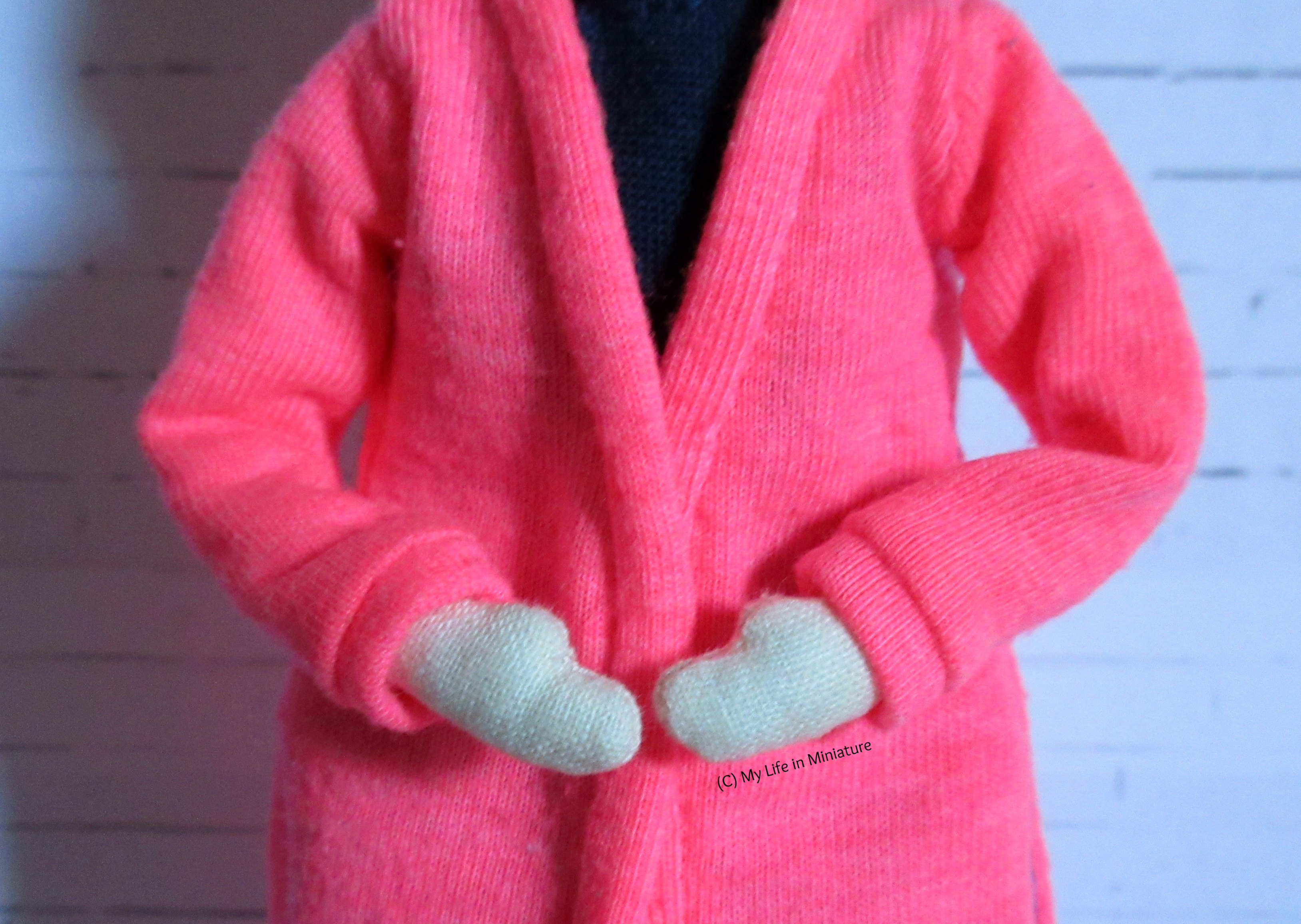 Tiffany wears the neon pink cardigan, her hands held in front of her. The cuffs of her sleeves are visible, as well as the binding around the front opening.