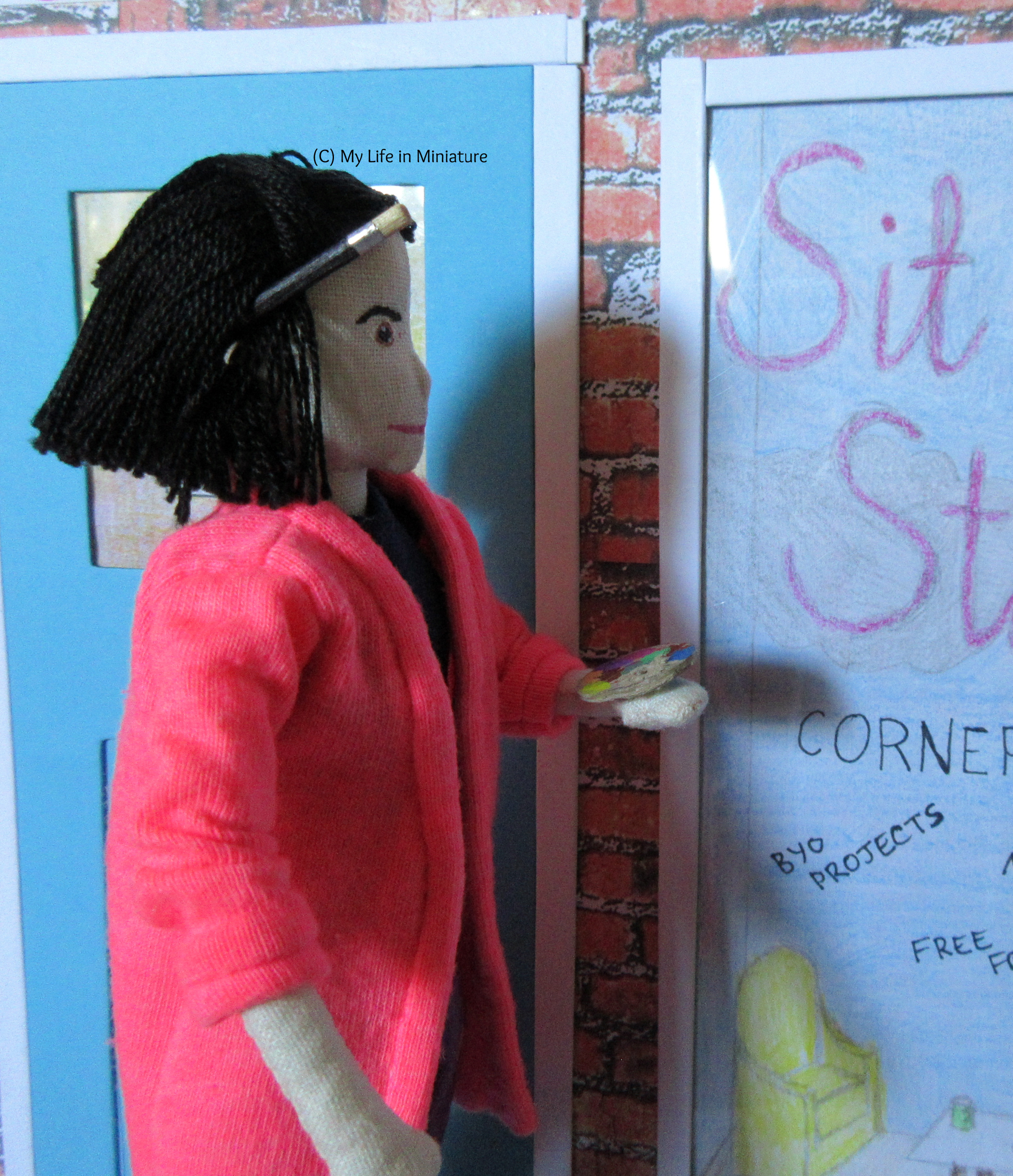 Tiffany stands on something, next to the frame of a front window. She has a paintbrush behind her ear, and holds a paint palette. She looks at the frame. 