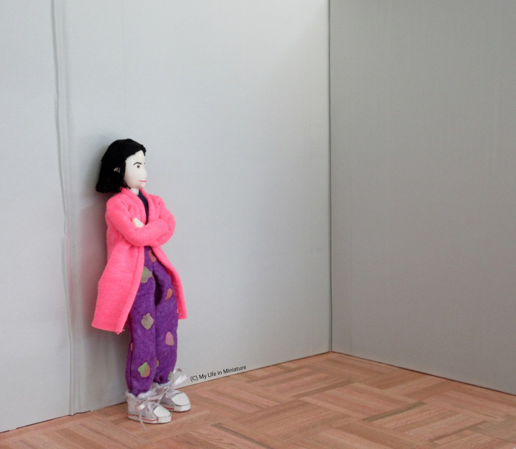 Tiffany stands in a grey-walled corner, arms crossed, deep in thought.