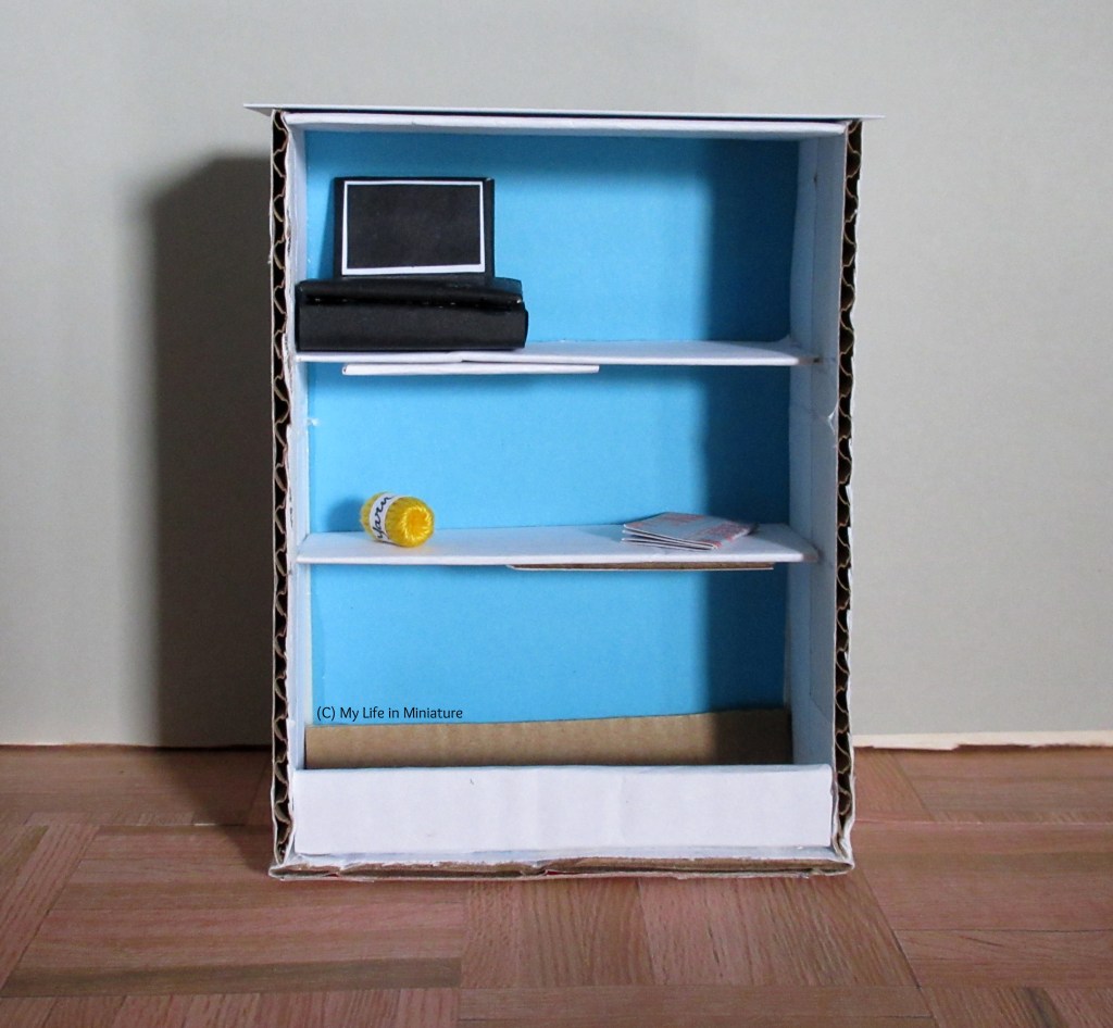Back of the counter. Two shelves hold the cash register, the magazine, and a ball of yellow yarn.