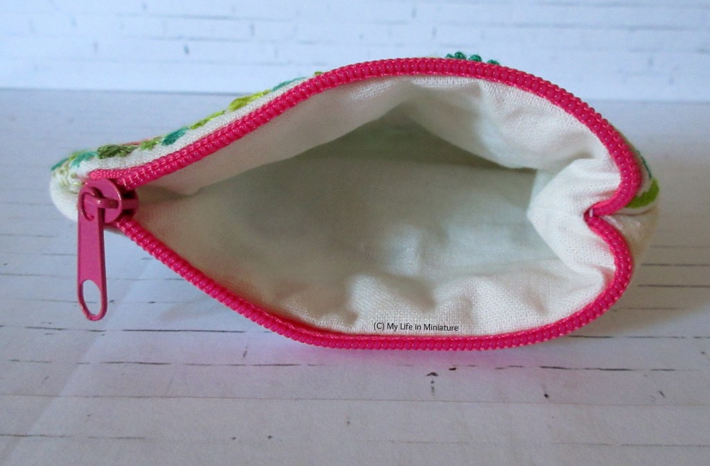 View of the plain white inside of the pouch, with bright pink zip unzipped.