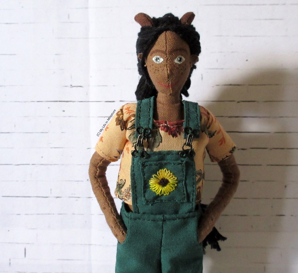 Petra wears the top under her green overalls against a white brick background.