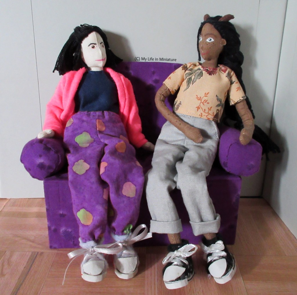 Petra and Tiffany sit side-by-side on the purple couch, looking at each other. 