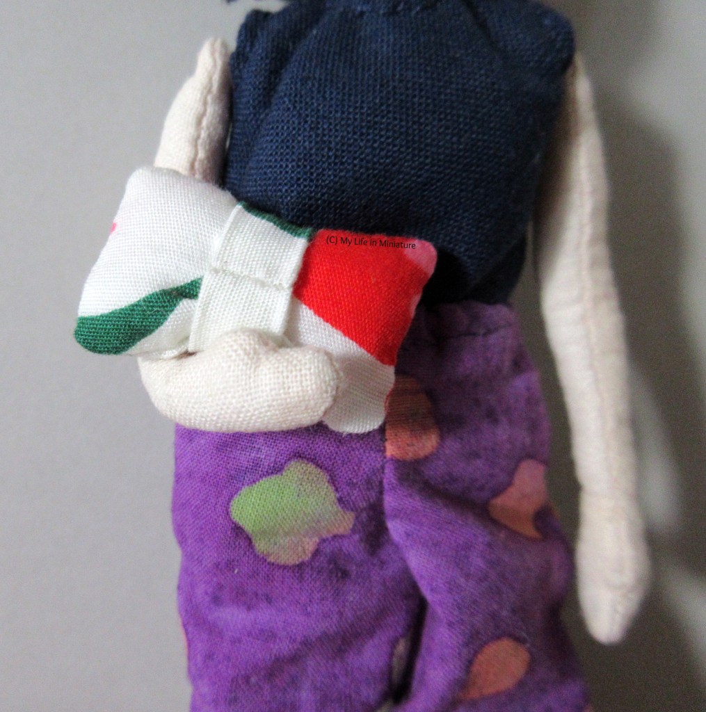 Close-up of Tiffany holding the bow tie cushion so the back is visible. Red and dark green splotches are visible, as well as the seam on the centre strip.