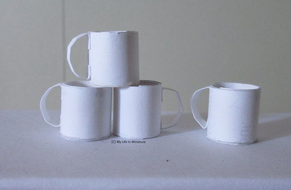 Four plain white mugs sit on a white surface. Three are stacked in a pyramid, and one sits to the right of the pyramid.