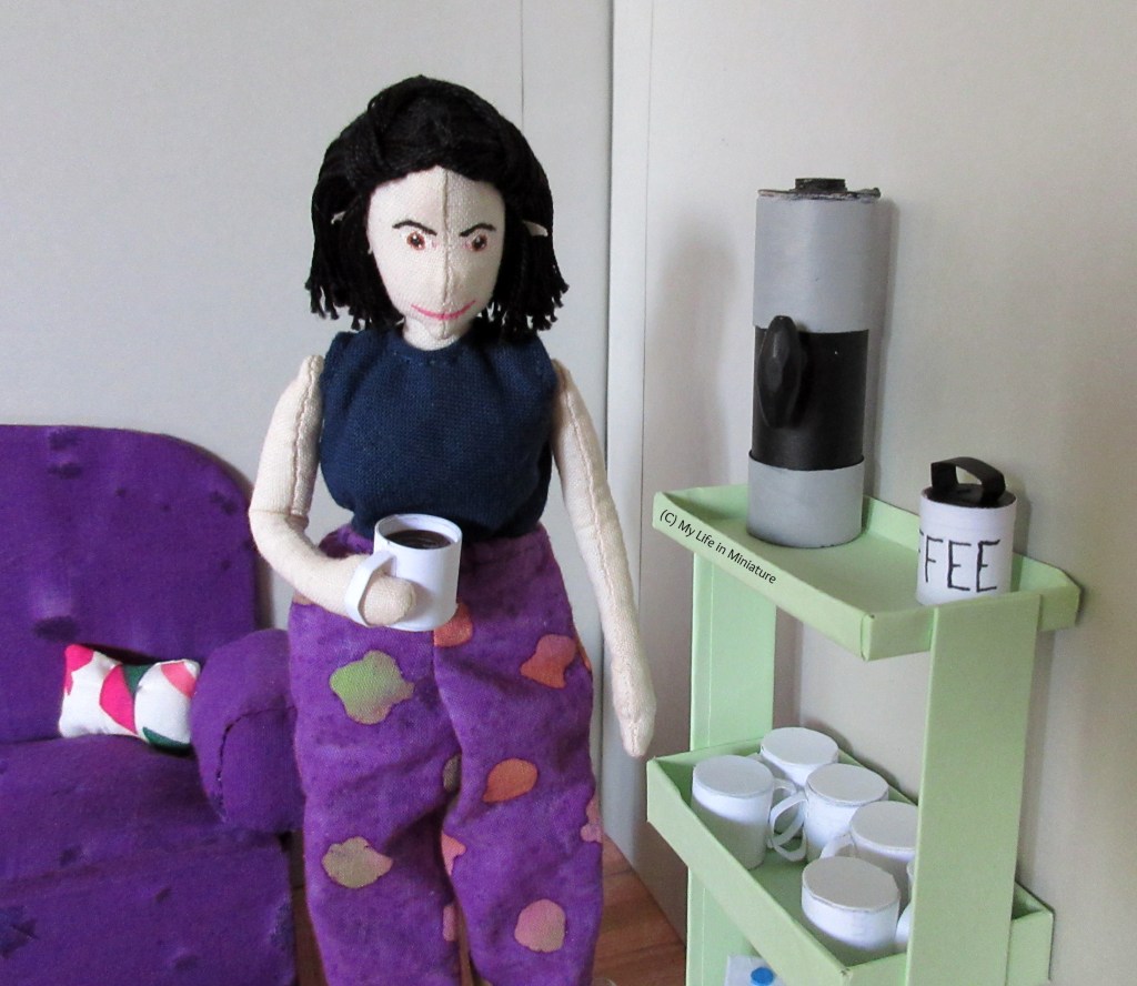 Tiffany stands next to the drinks trolley, holding a freshly made cup of coffee. She looks down at the cup, smiling.