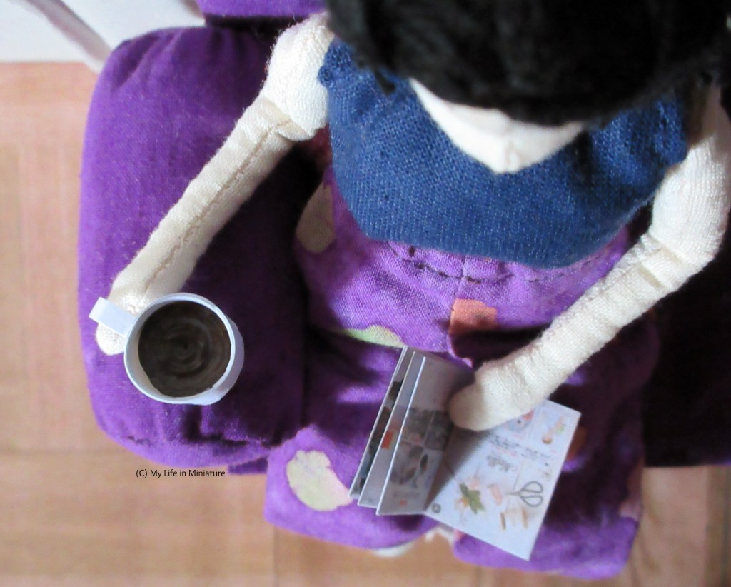 Above view of Tiffany sitting on the purple couch. She has an open magazine in her lap, and the mug of coffee is on the arm of the couch. 