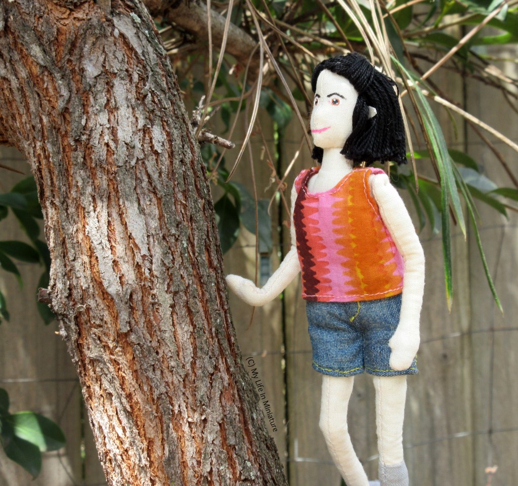 Tiffany stands in a tree fork, one hand on a branch for stability. She looks up the branch at something out of shot.