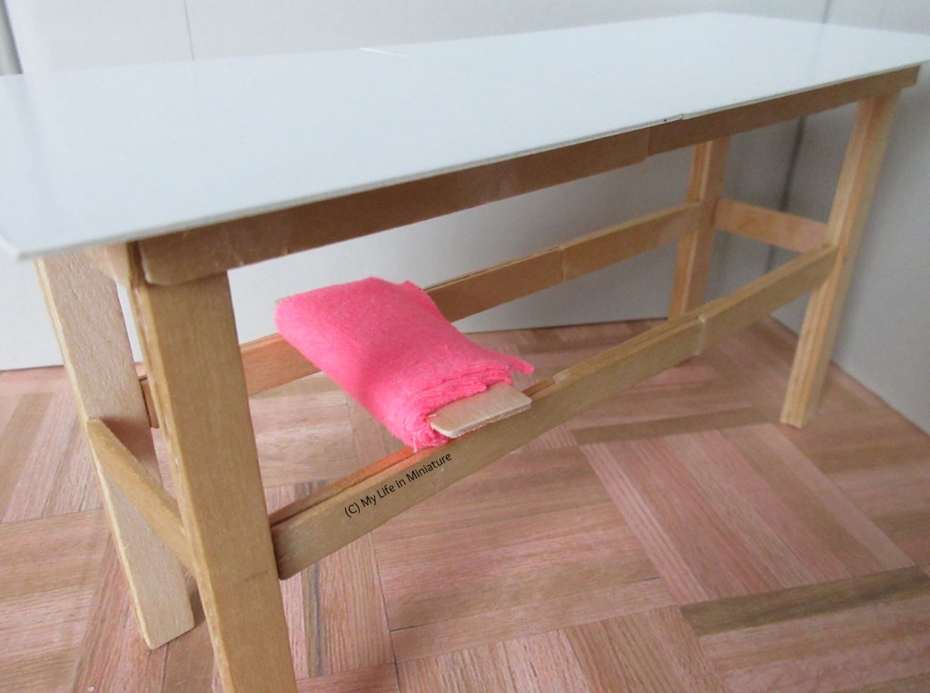 Close-up of a bolt of bright pink fabric resting across two horizontal supports attached to the legs of the table. 