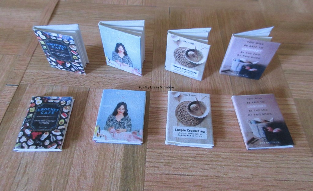 The four different craft books sit on a wood parquet background. Each book has a flat version lying down in front, and an openable version with pages standing upright behind.